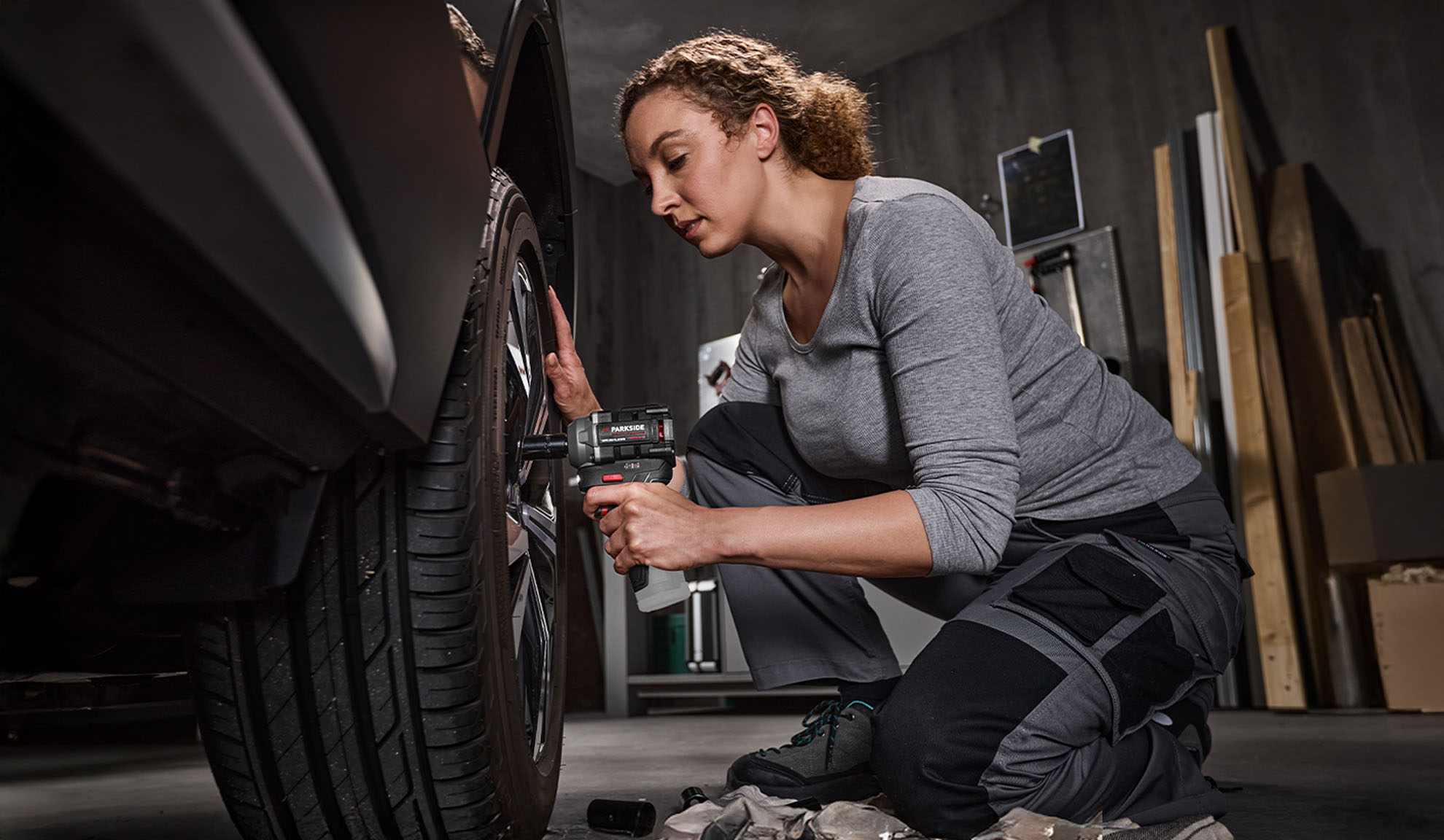 Femme utilisant une clé à chocs Parkside pour changer un pneu de voiture dans un garage.
