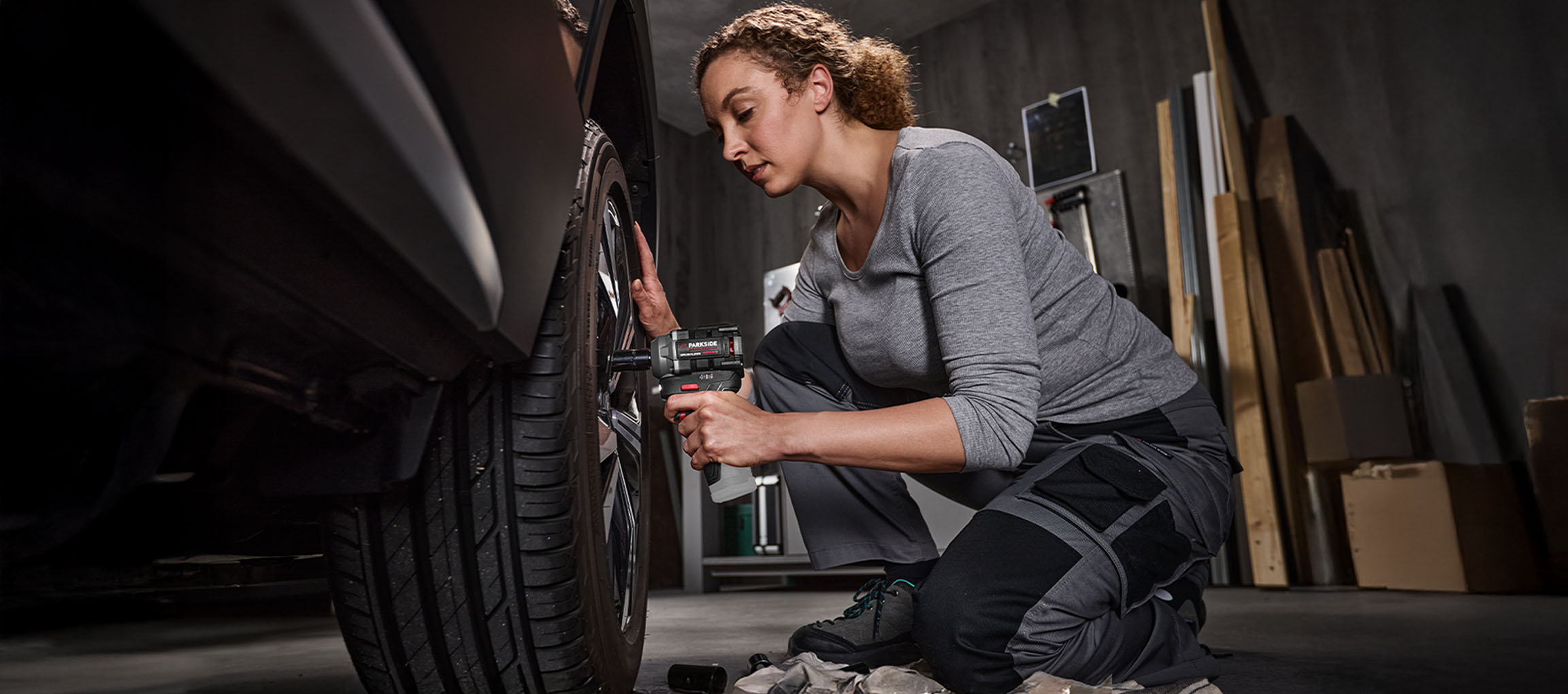Femme utilisant une clé à chocs Parkside pour changer un pneu de voiture dans un garage.