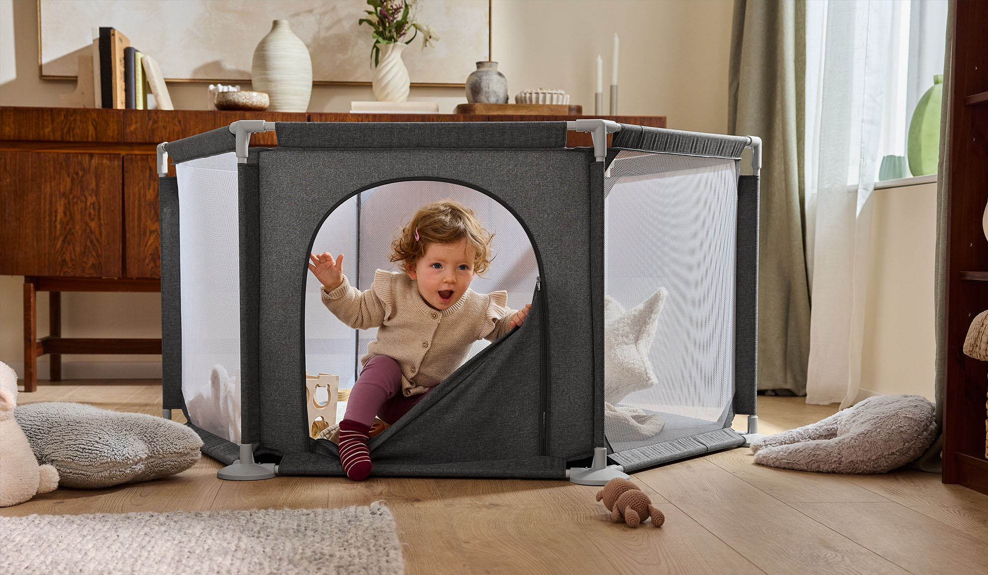 Bébé heureux sortant d'un parc gris dans un salon confortable.