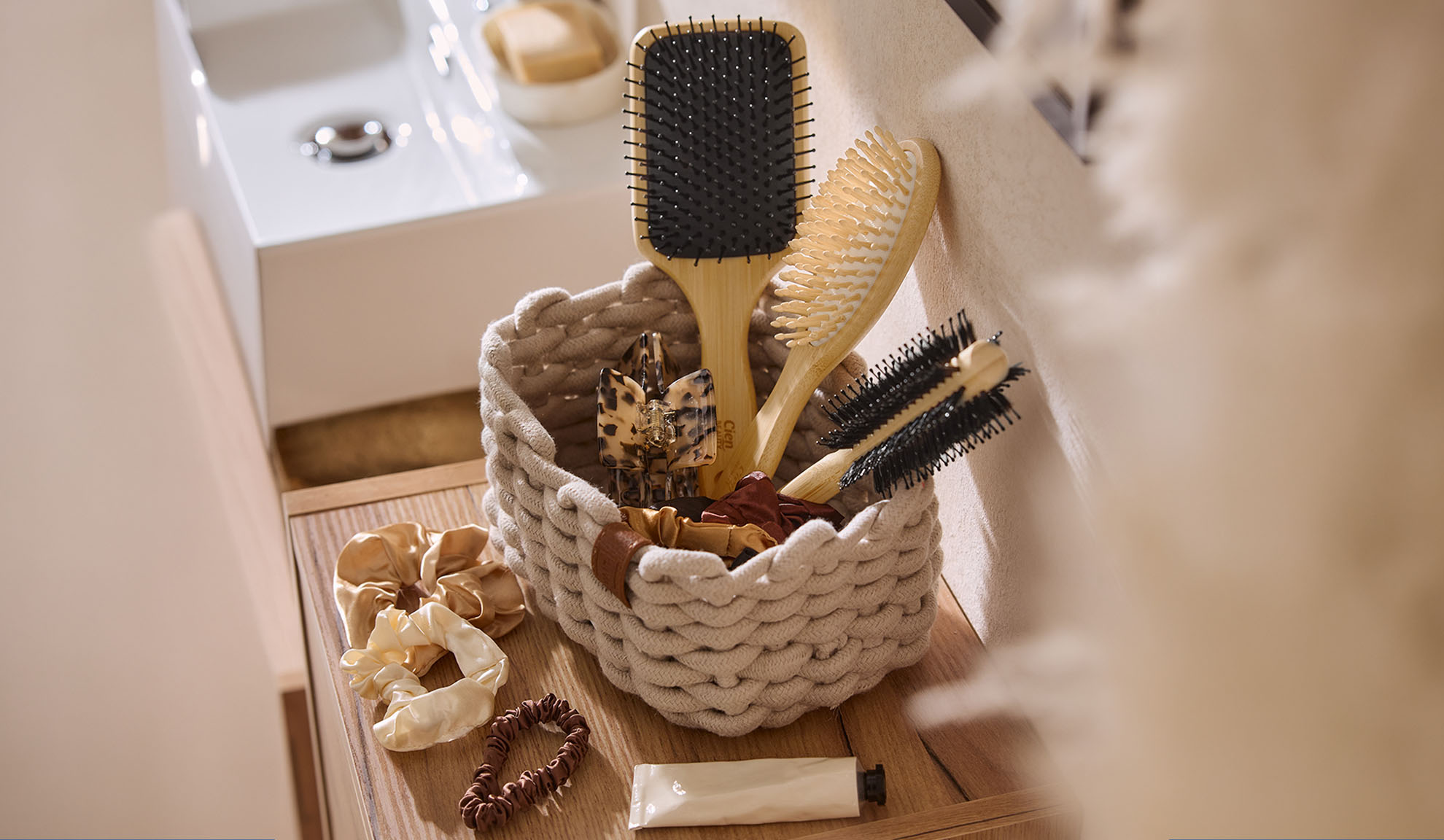 Panier en corde avec brosses à cheveux en bois, pinces et chouchous dans une salle de bain.