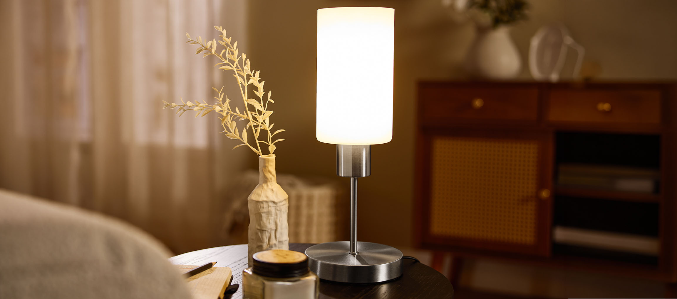 Lampe de table avec un vase et des plantes séchées sur une table de chevet.