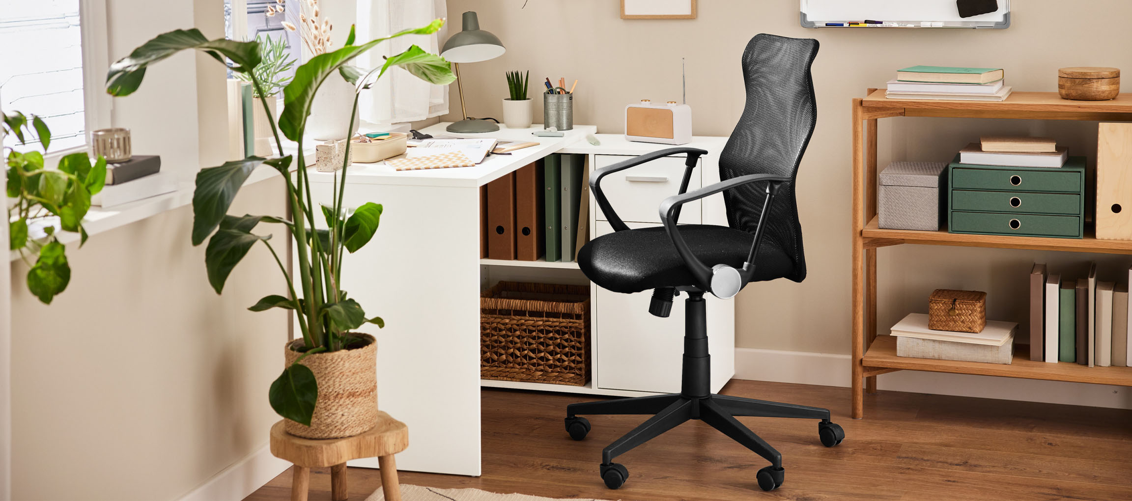 Un bureau à domicile avec un bureau blanc, une chaise de bureau noire et une étagère en bois.