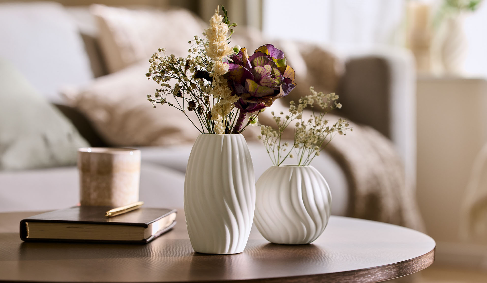 Vases blancs avec fleurs séchées sur une table basse en bois dans un salon douillet.