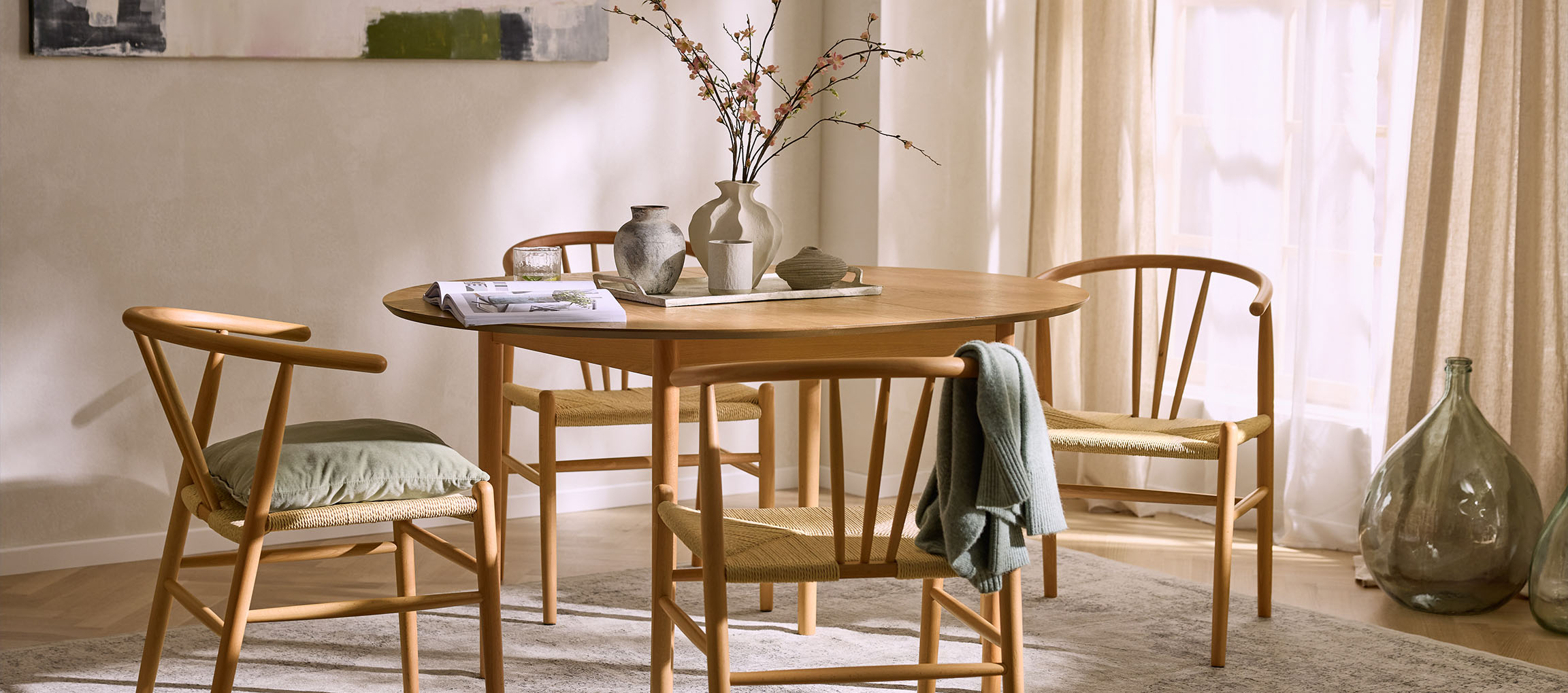 Salle à manger avec table ronde en bois, chaises en bois avec assises en corde et vases décoratifs.