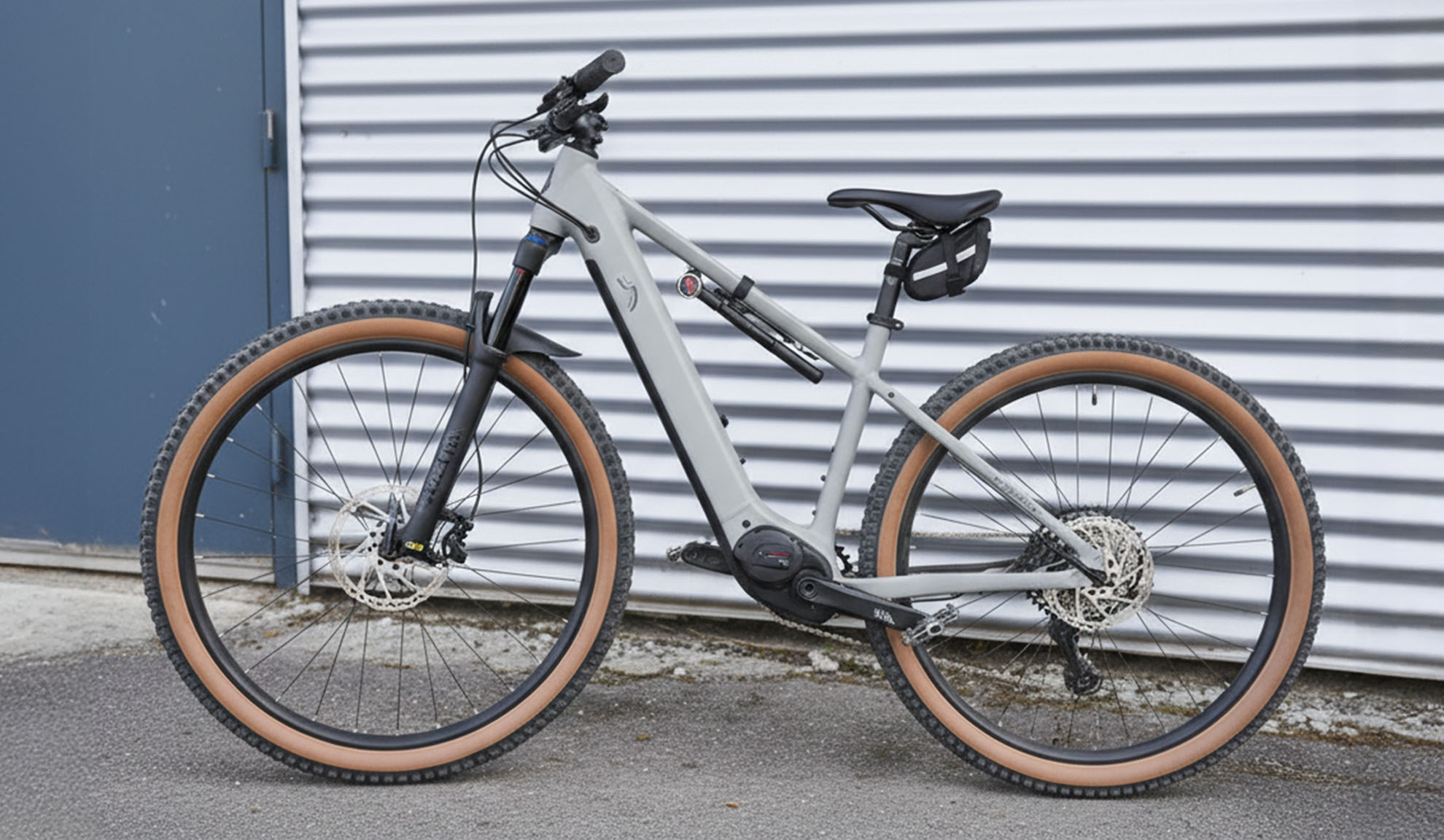 VTT électrique gris avec pneus marron, garé devant un mur en tôle ondulée.