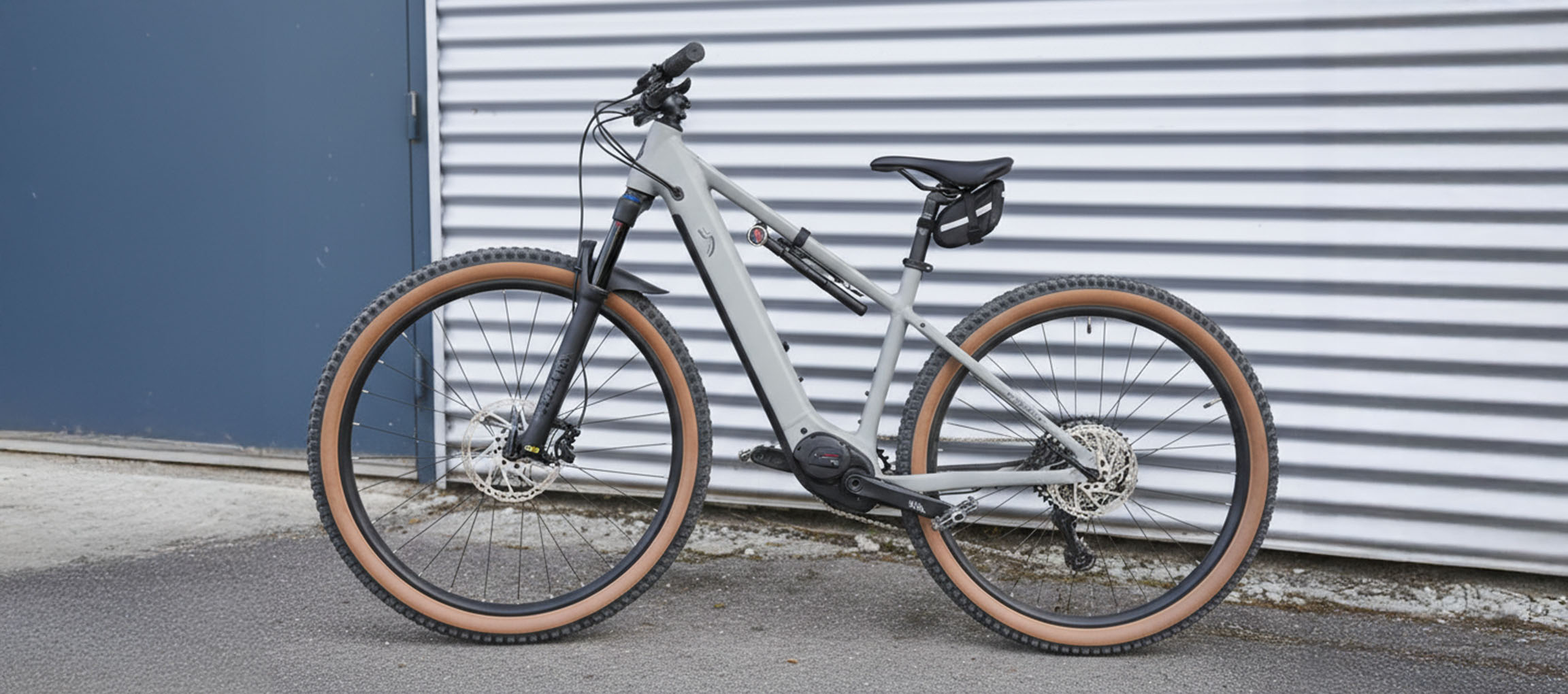 VTT électrique gris avec pneus marron, appuyé contre un mur ondulé.