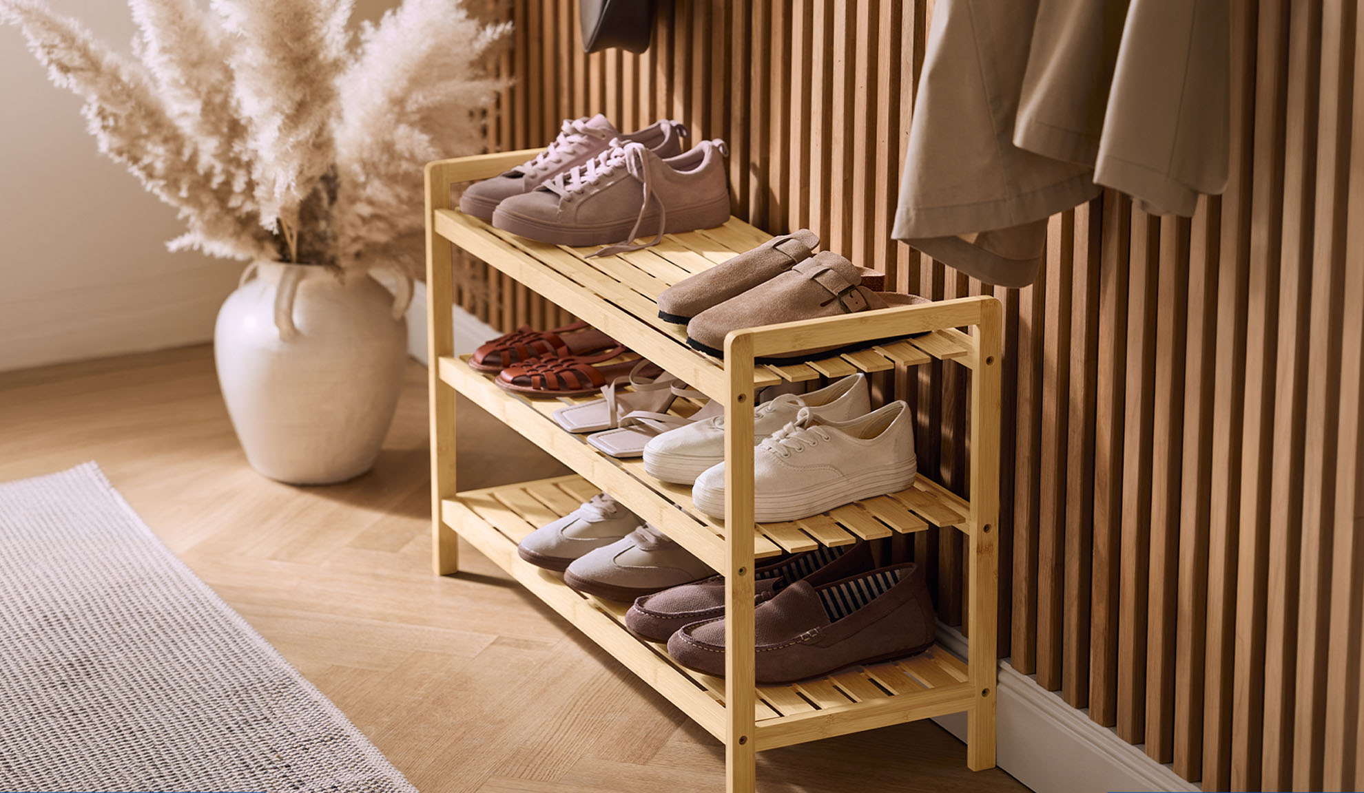 Étagère à chaussures en bois avec diverses chaussures et un vase d'herbe de la pampa dans un couloir.
