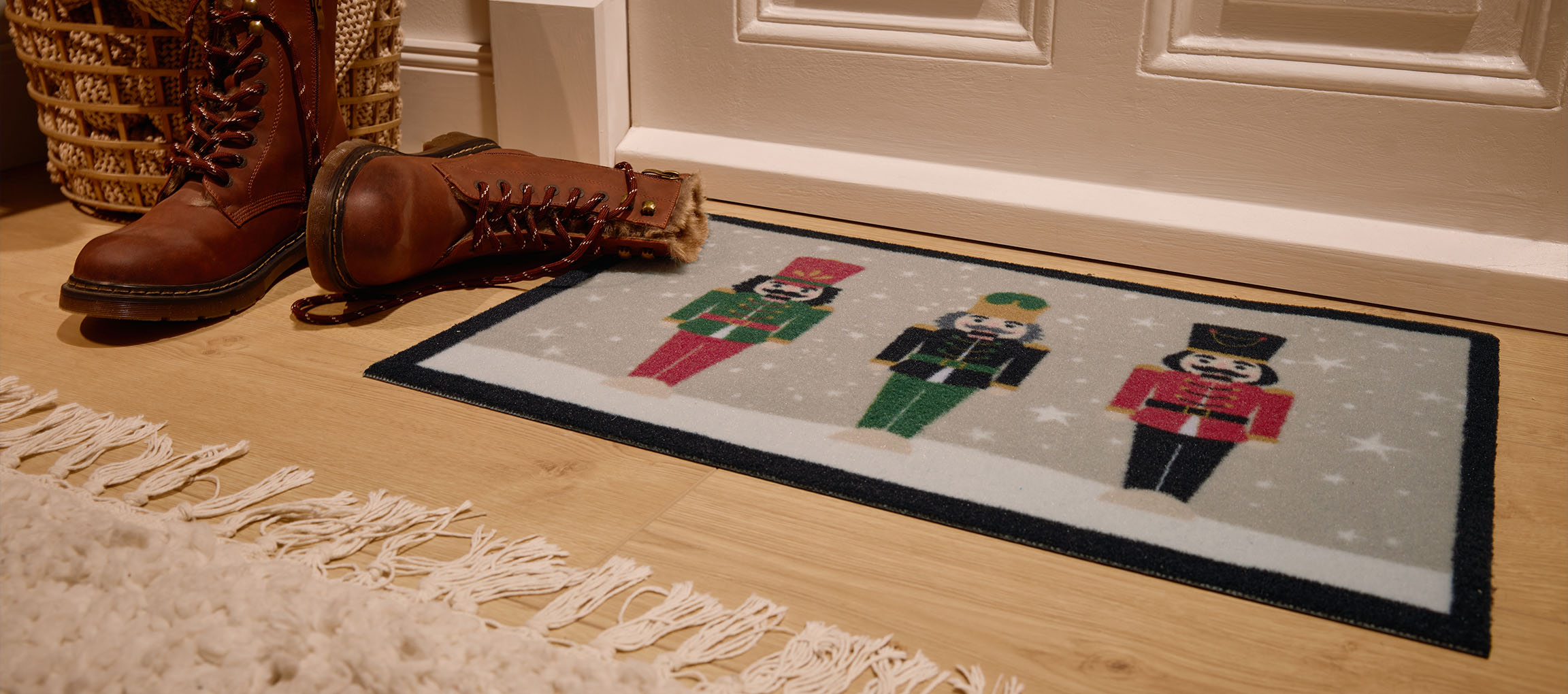 Paillasson de Noël casse-noisette, bottes marron et panier en osier à l'entrée.