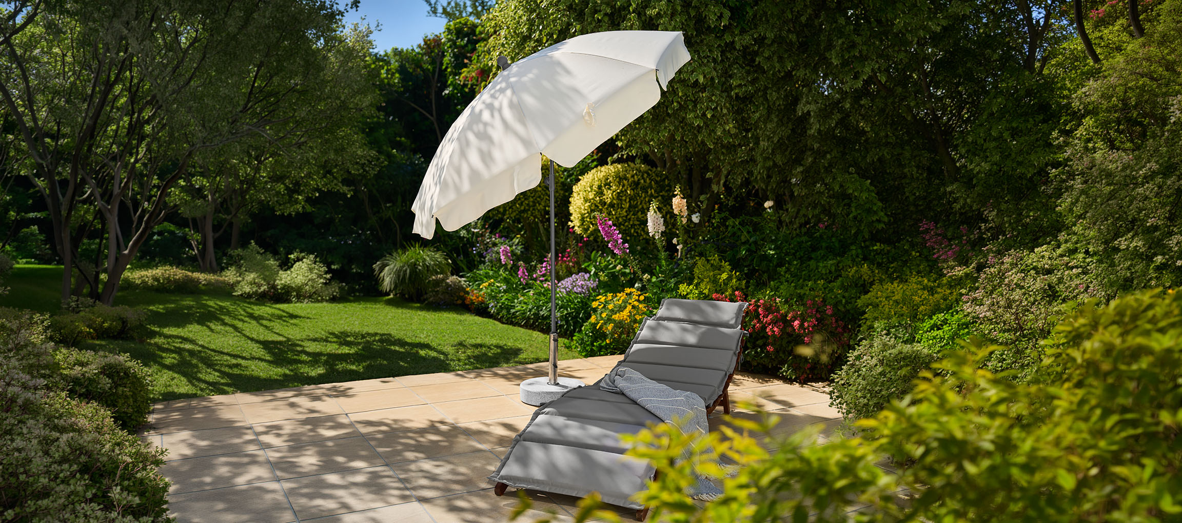 Transat de jardin avec parasol sur une terrasse, entouré de verdure et de fleurs.