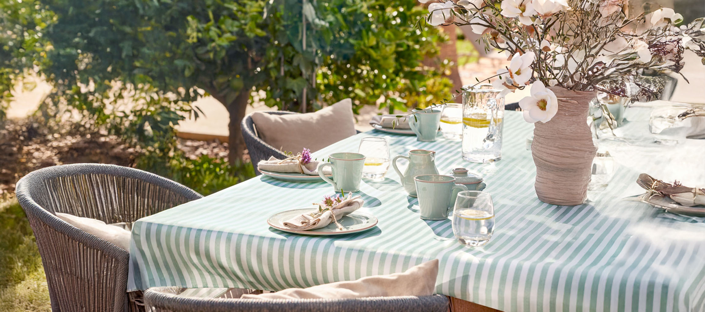 Table à manger extérieure avec nappe rayée, vaisselle en céramique vert menthe et fleurs.