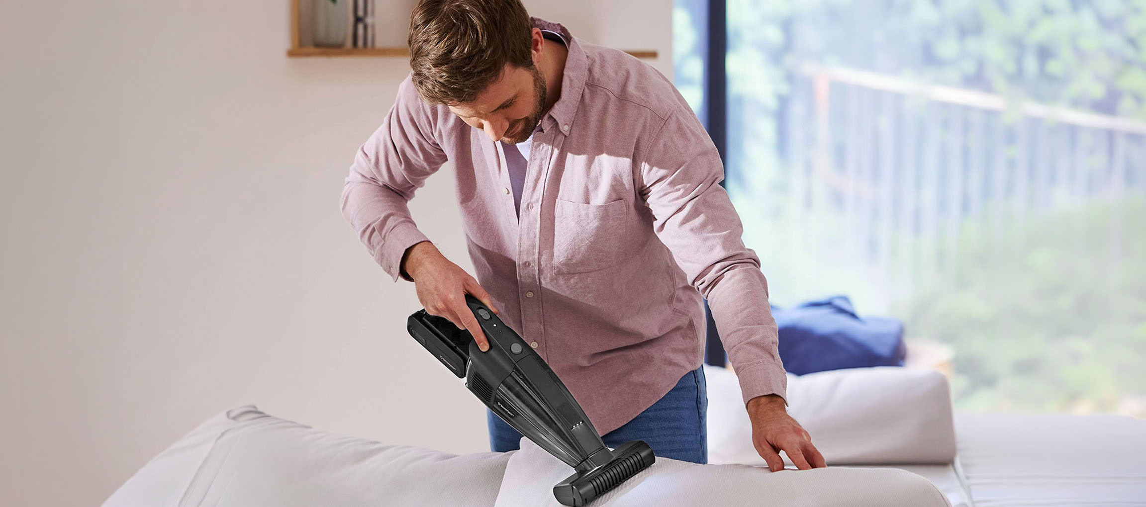 Homme nettoyant un canapé avec un aspirateur à main.
