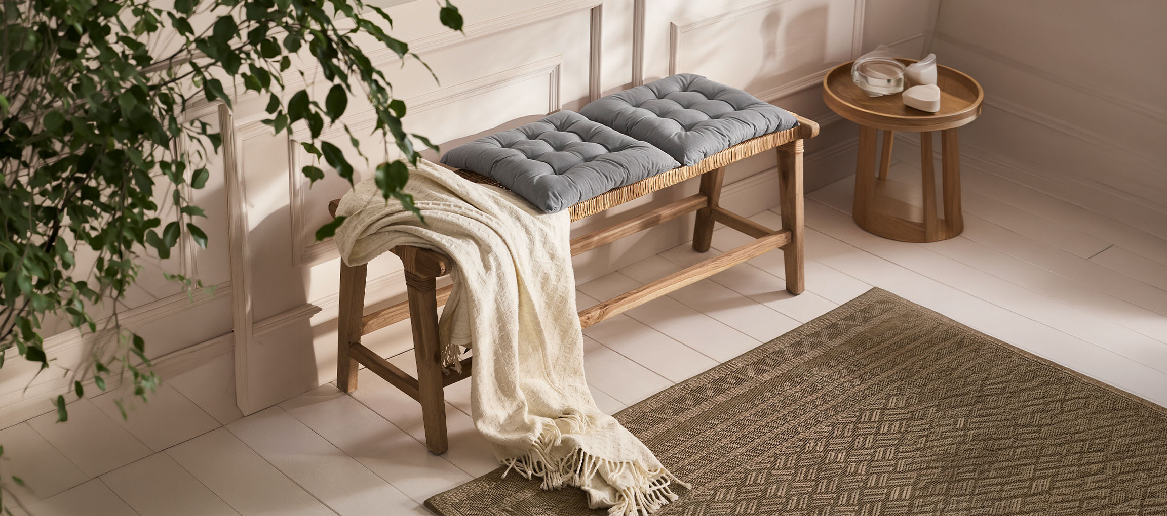 Banc en bois avec coussins gris et plaid blanc sur un parquet clair avec un tapis.