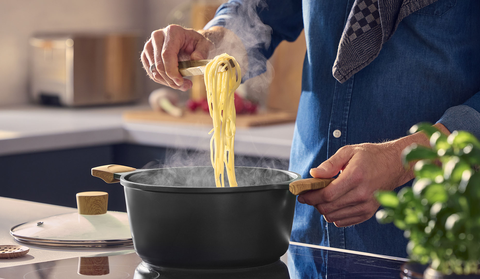 Homme soulevant des spaghettis fumants d'une casserole noire avec des poignées en bois.