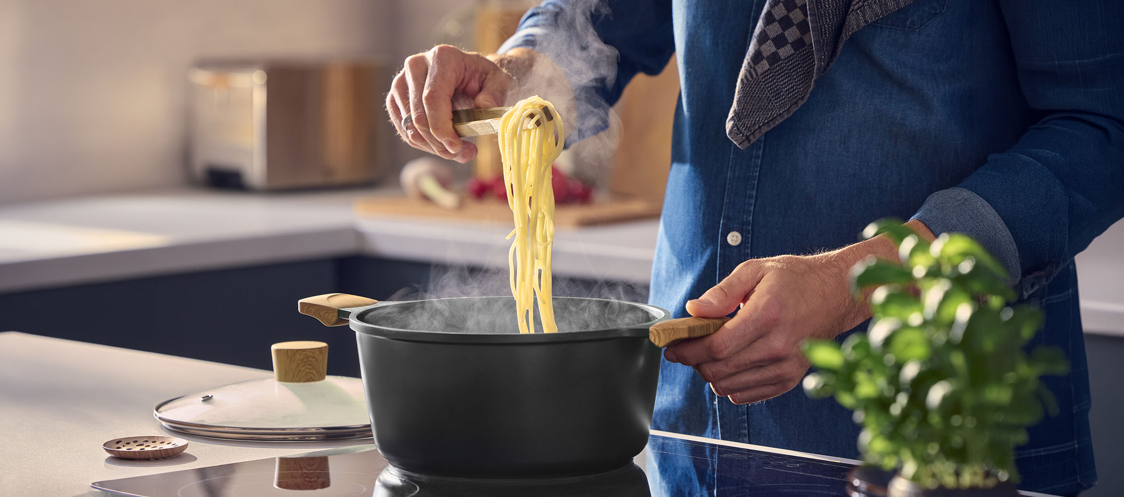 Homme cuisinant des pâtes dans une casserole noire avec des poignées en bois, utilisant des pinces en bois.
