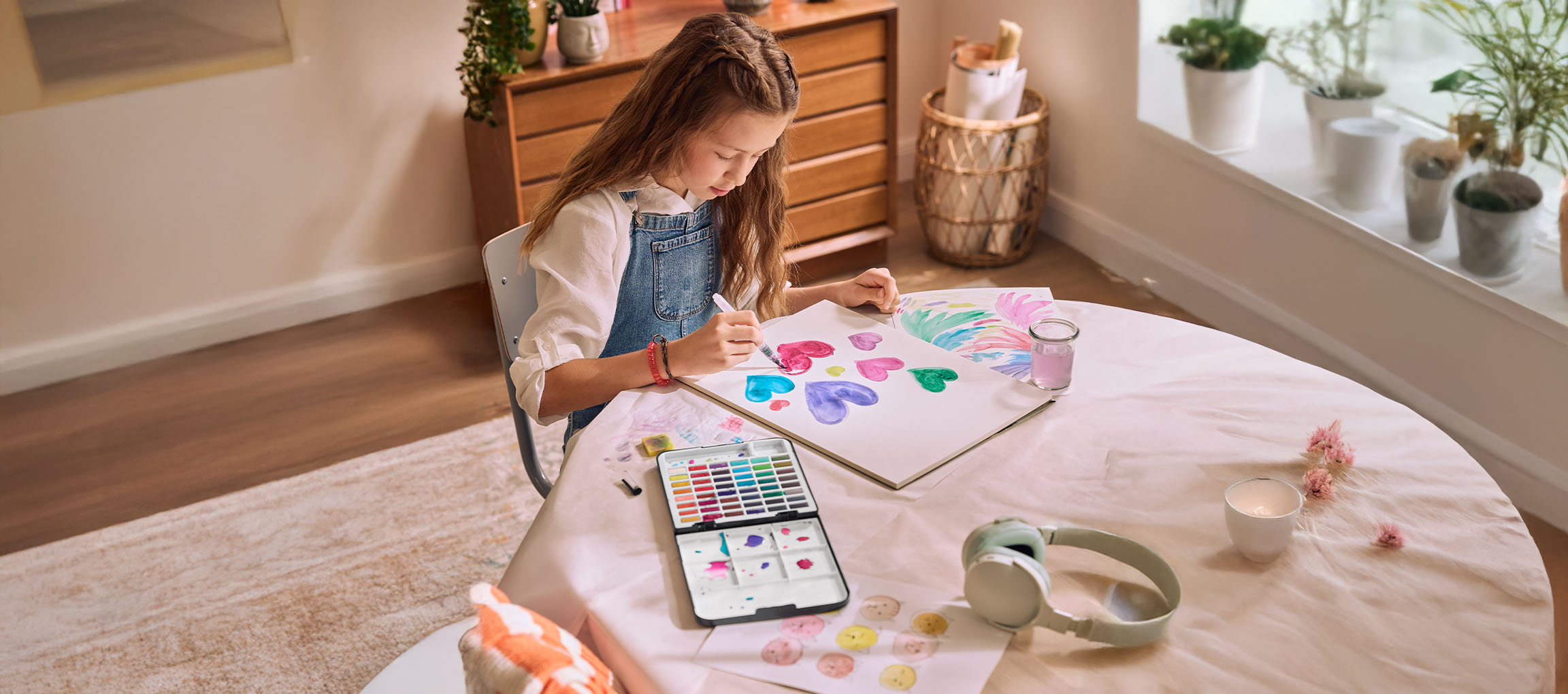 Une fille peint des cœurs à l'aquarelle à une table, avec une tablette affichant une palette de couleurs.