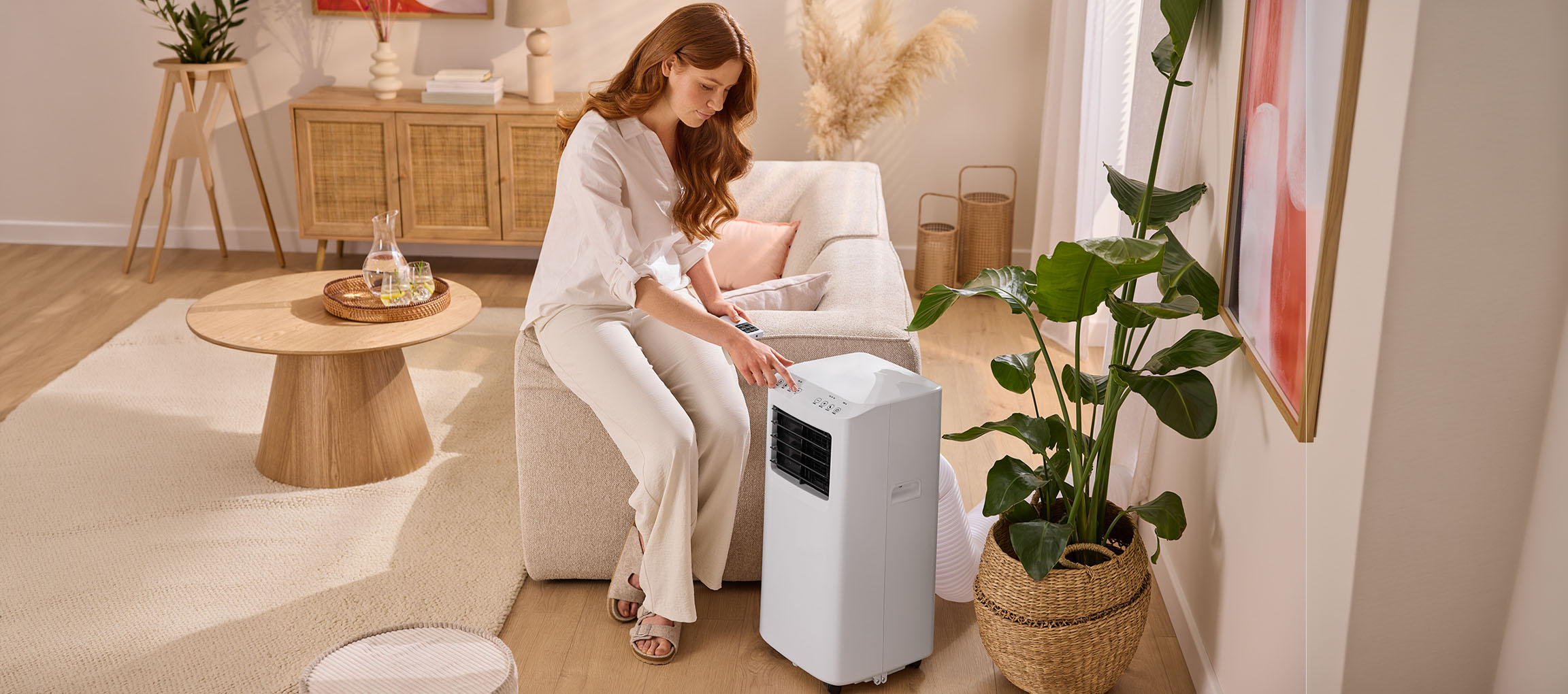 Femme ajustant un climatiseur portable dans un salon avec un canapé et une table basse.