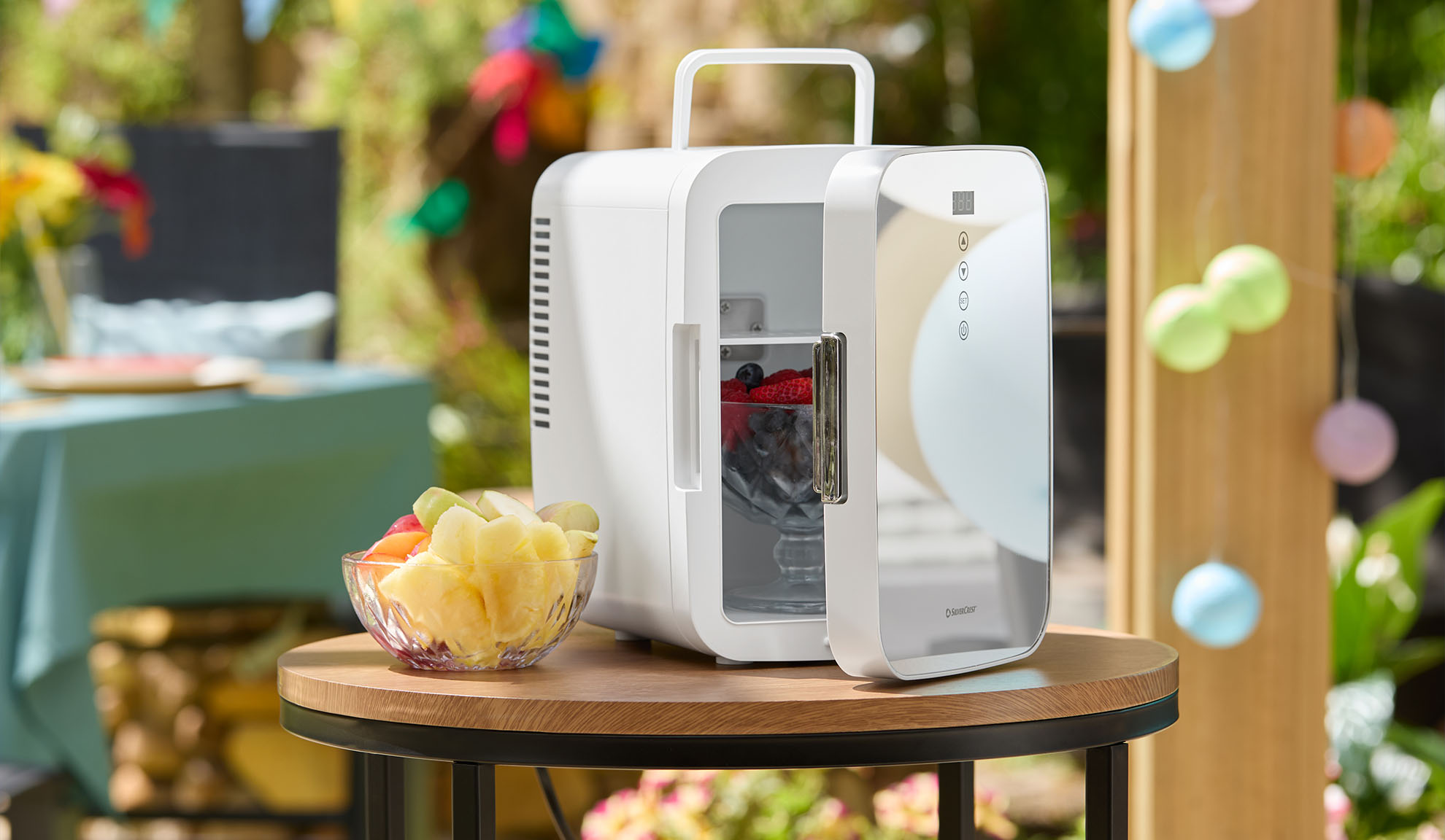 Mini-réfrigérateur portable avec des fruits sur une table en bois à l'extérieur.
