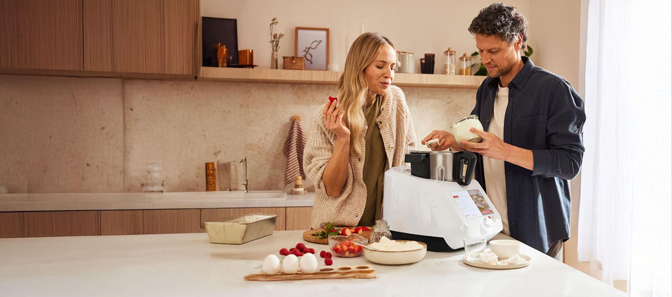 Un couple cuisine ensemble avec un robot de cuisine moderne dans une cuisine lumineuse.