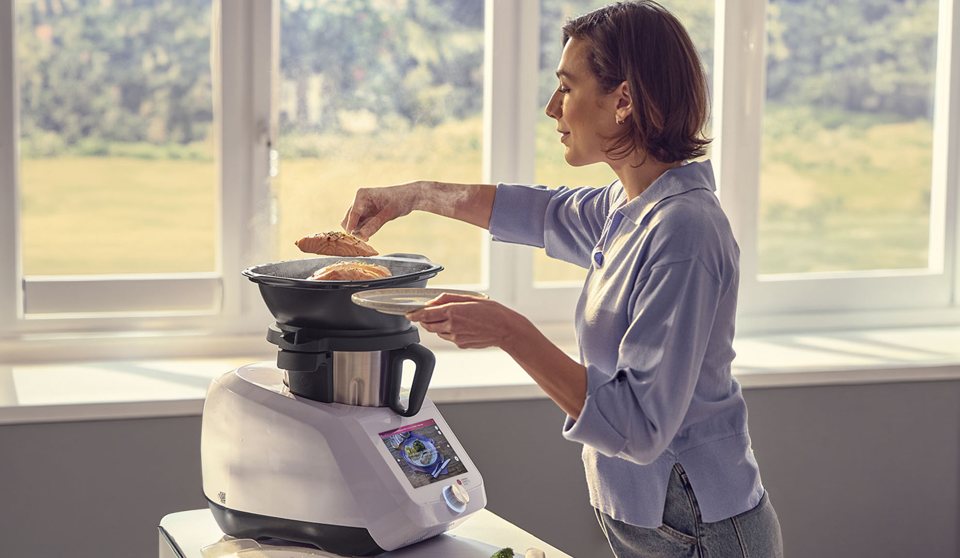 Femme cuisinant du saumon dans un robot de cuisine avec fonction vapeur, utilisant l'écran numérique.