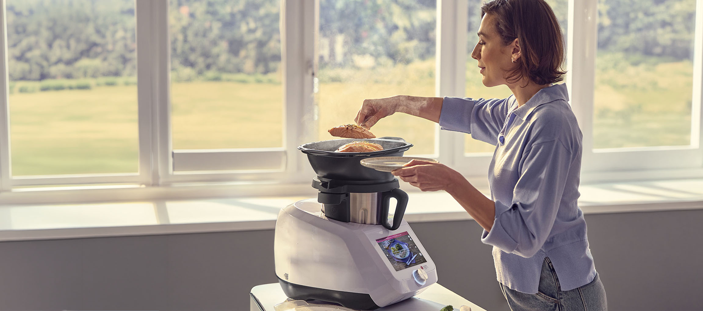 Femme cuisinant avec un robot de cuisine, avec accessoire vapeur et saumon.