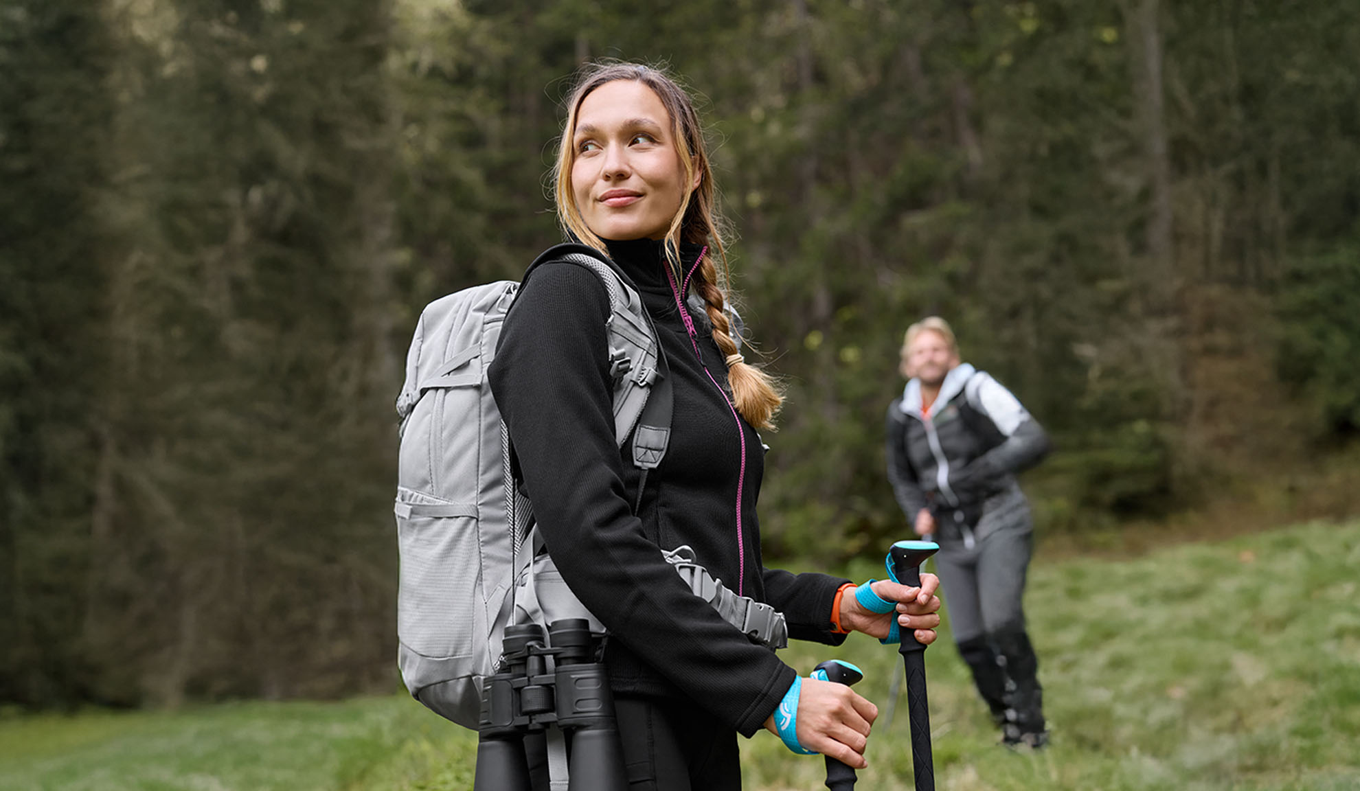 Femme avec sac à dos de randonnée et bâtons de trekking, homme en arrière-plan.