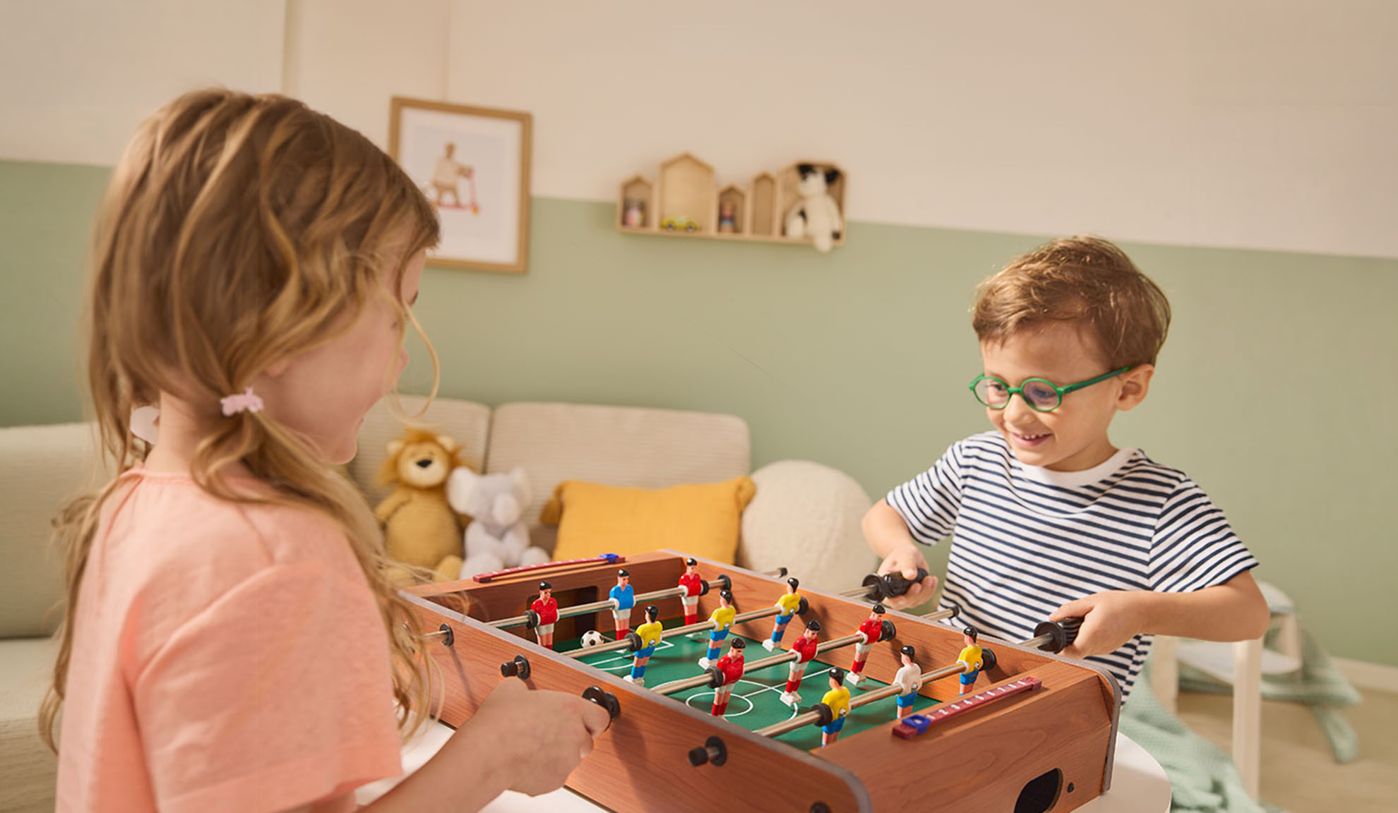 Deux enfants jouent au baby-foot, riant joyeusement.