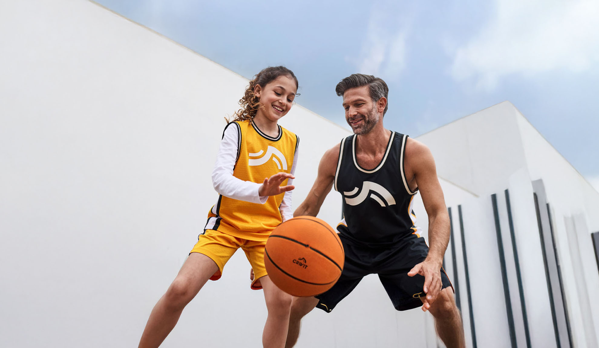 Père et fille jouant au basket en maillots et shorts Crivit.