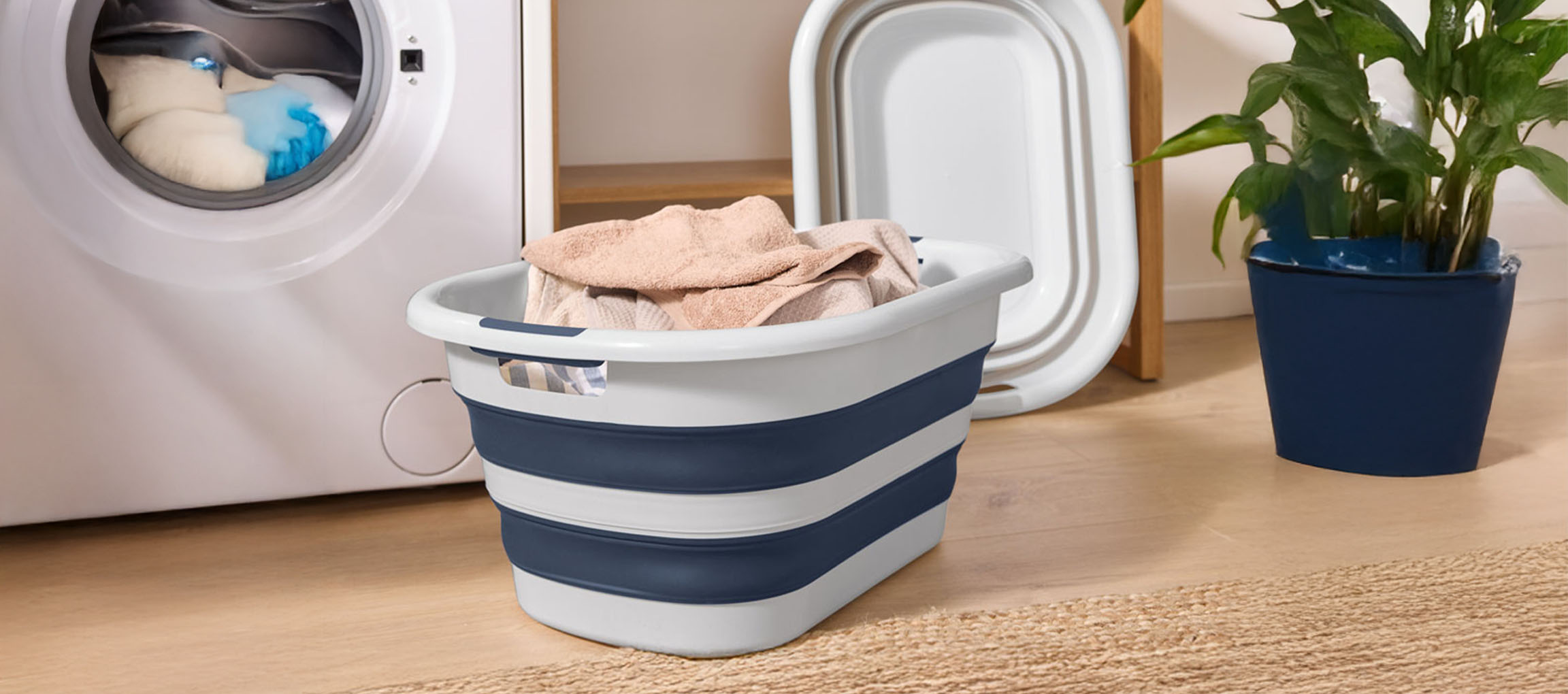 Une machine à laver blanche avec un panier à linge pliable bleu et blanc rempli de serviettes.