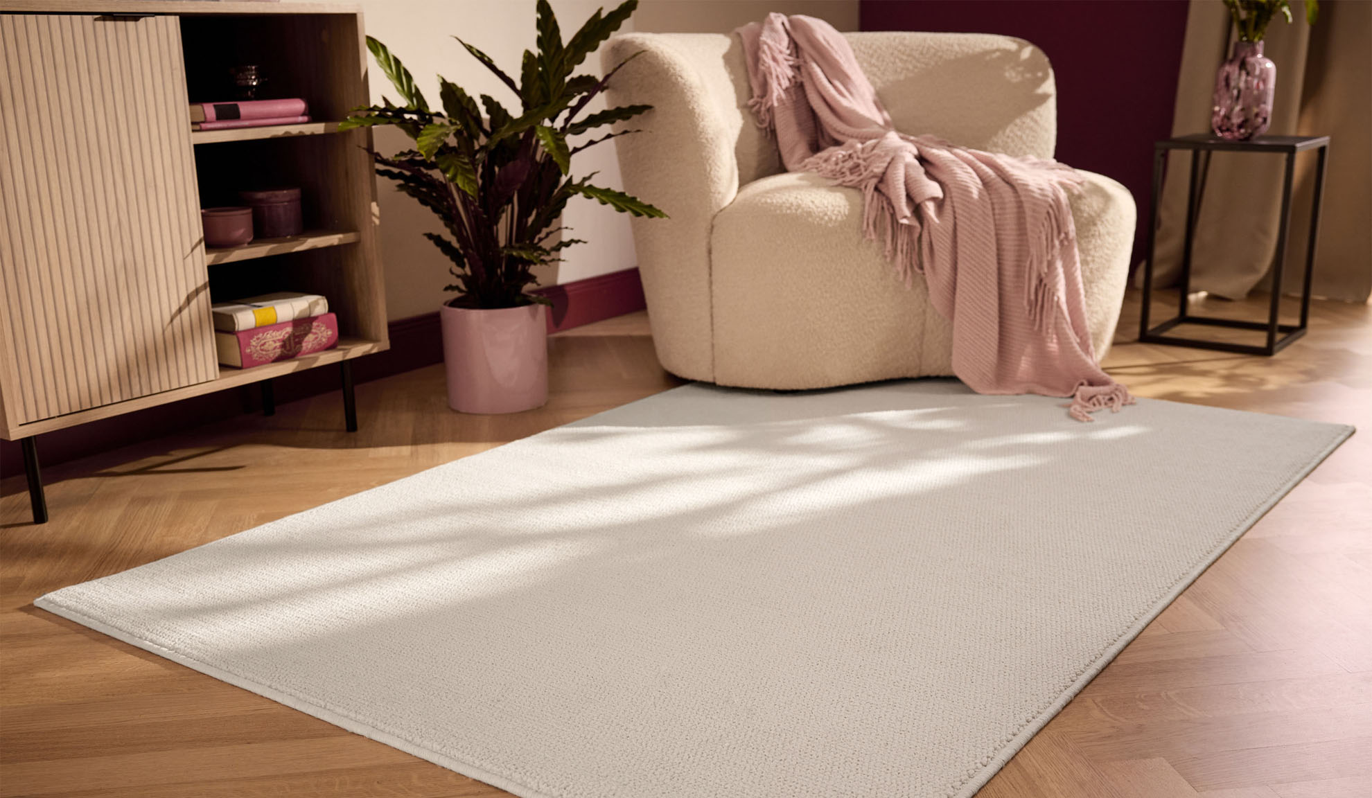 Salon avec tapis crème, fauteuil, plante et meuble en bois.