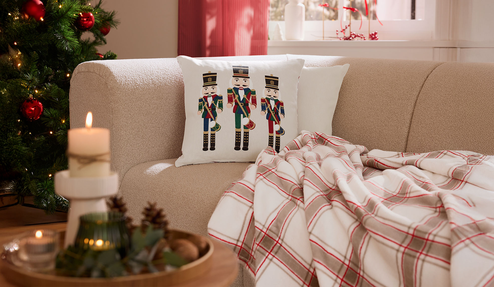 Salon de Noël avec canapé, coussins casse-noisettes, plaid à carreaux et bougies.