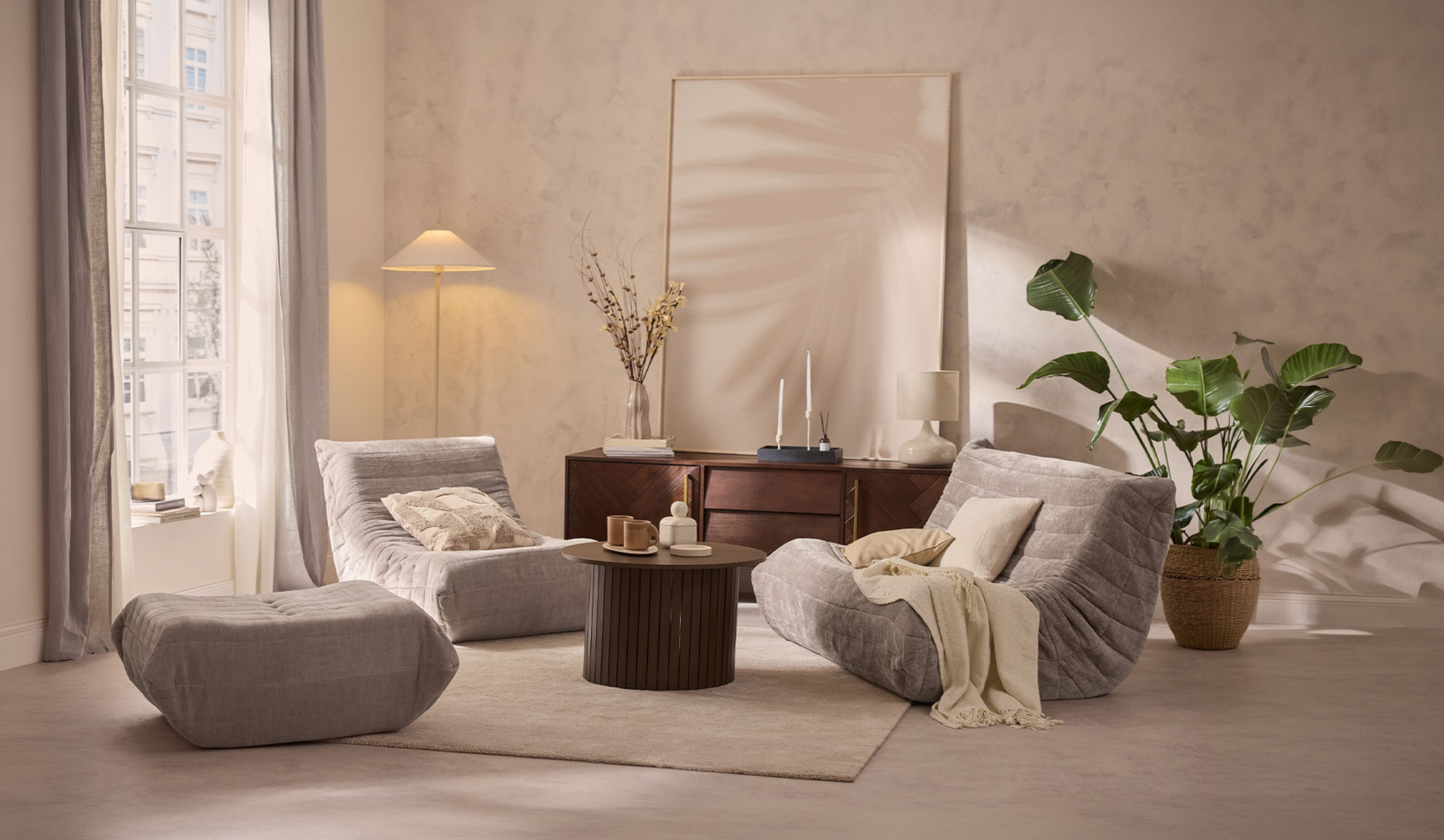 Salon confortable avec deux fauteuils gris, un pouf, une table basse et une plante.