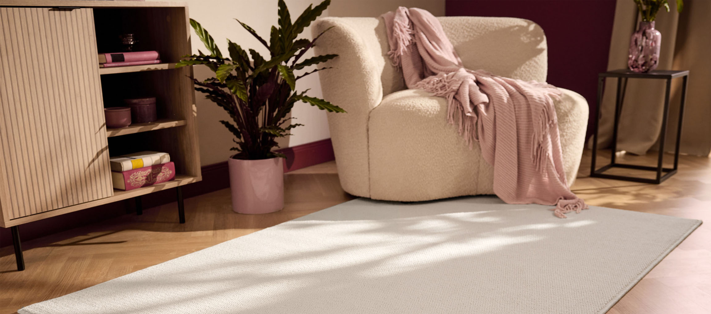 Un tapis clair sur un parquet, avec un fauteuil beige et un meuble en bois.