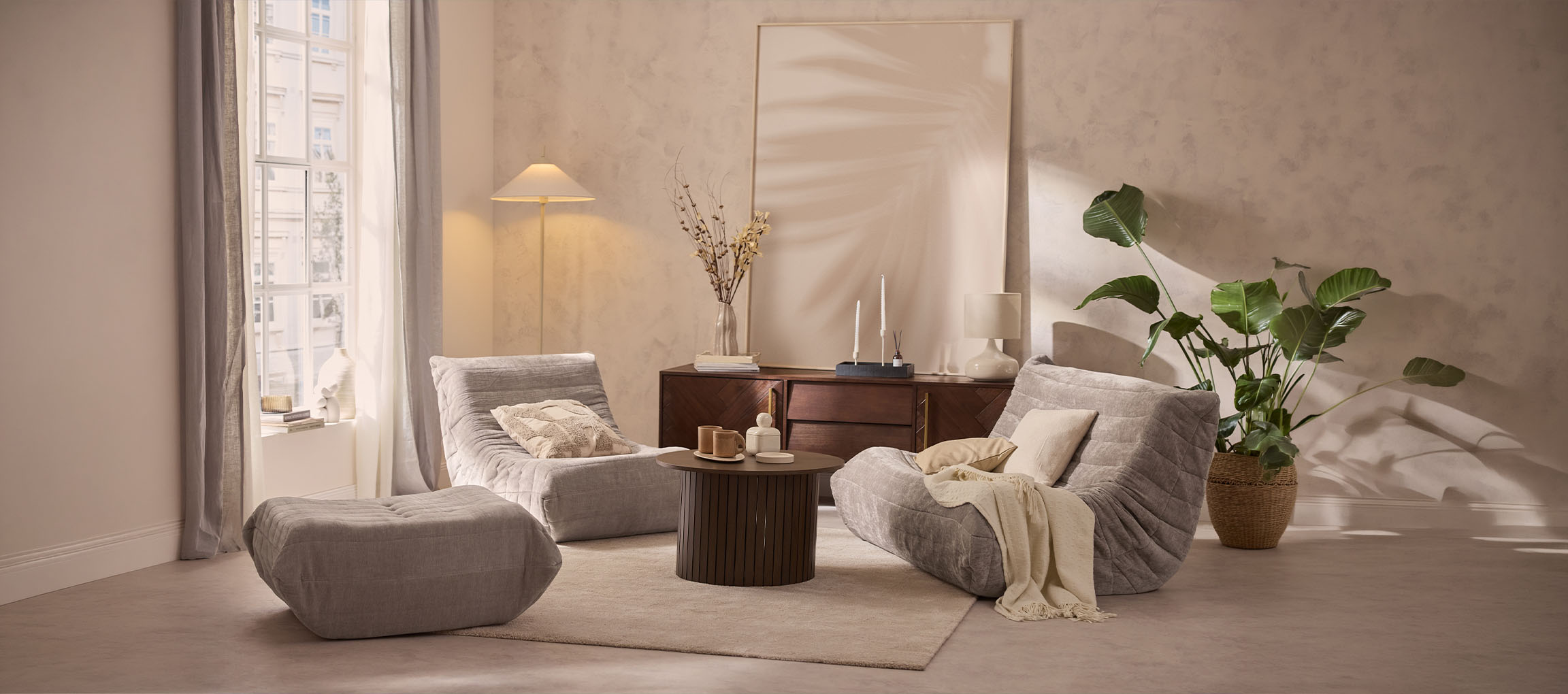 Salon confortable avec deux fauteuils gris, un pouf et une table en bois.