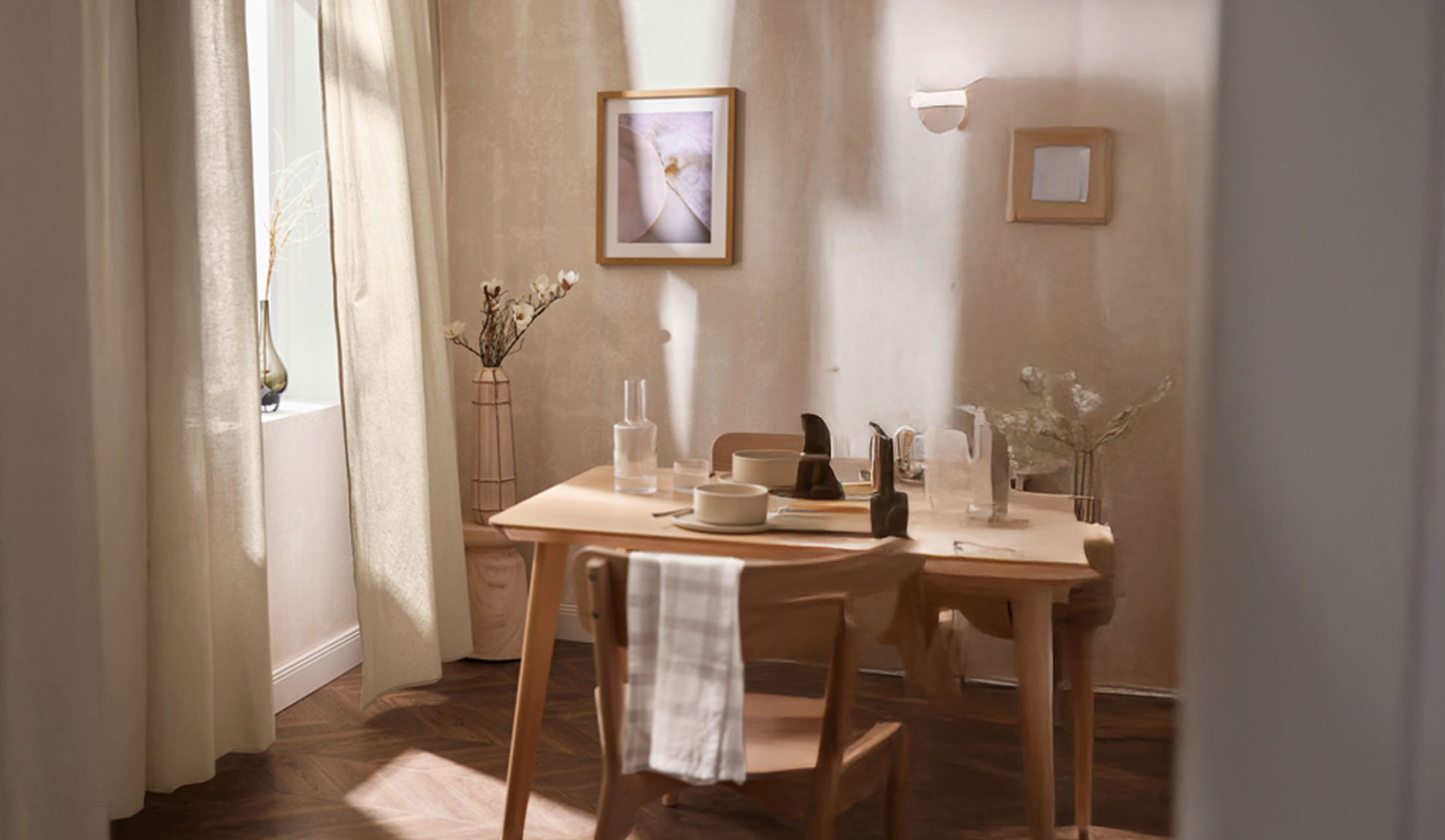 Une salle à manger avec une table en bois dressée pour deux, avec un décor clair et une lumière naturelle.