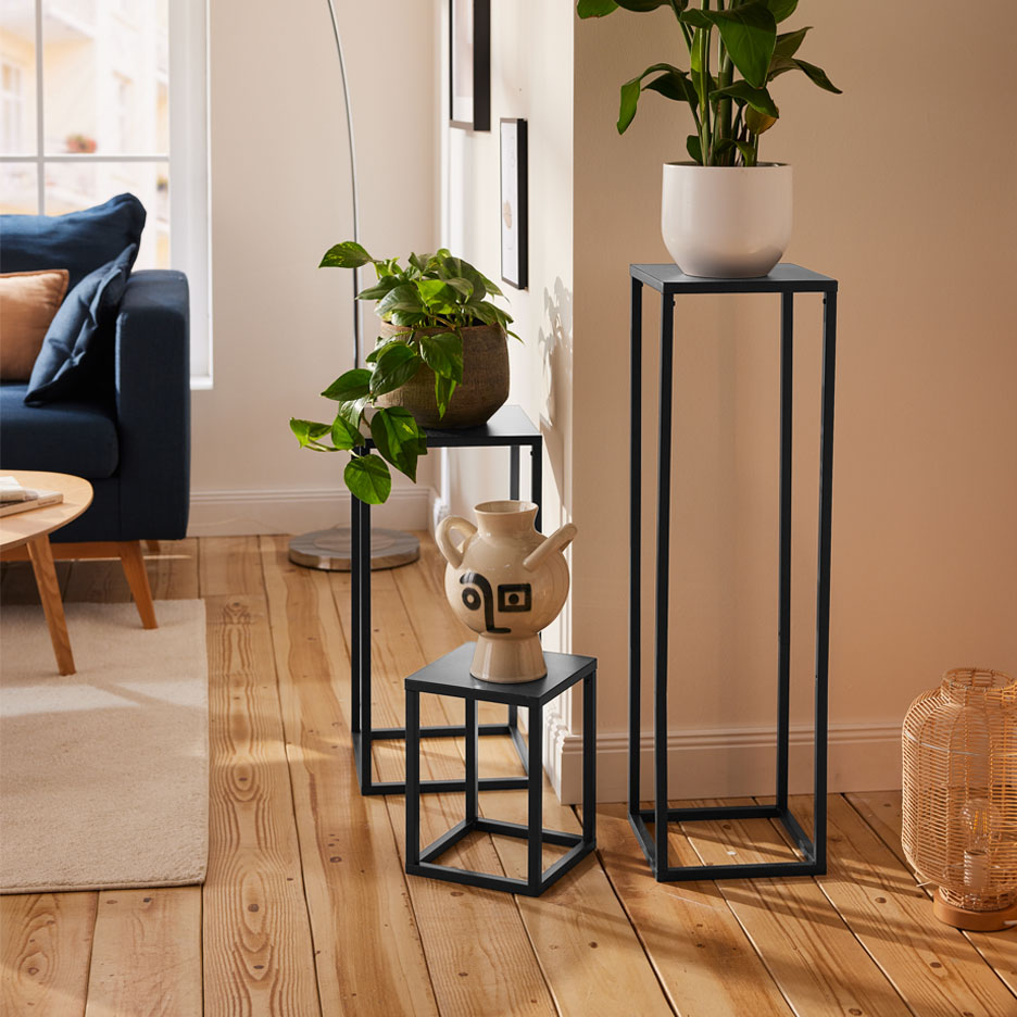 Trois supports à plantes noirs élégants exposent des plantes et un vase dans un salon moderne.