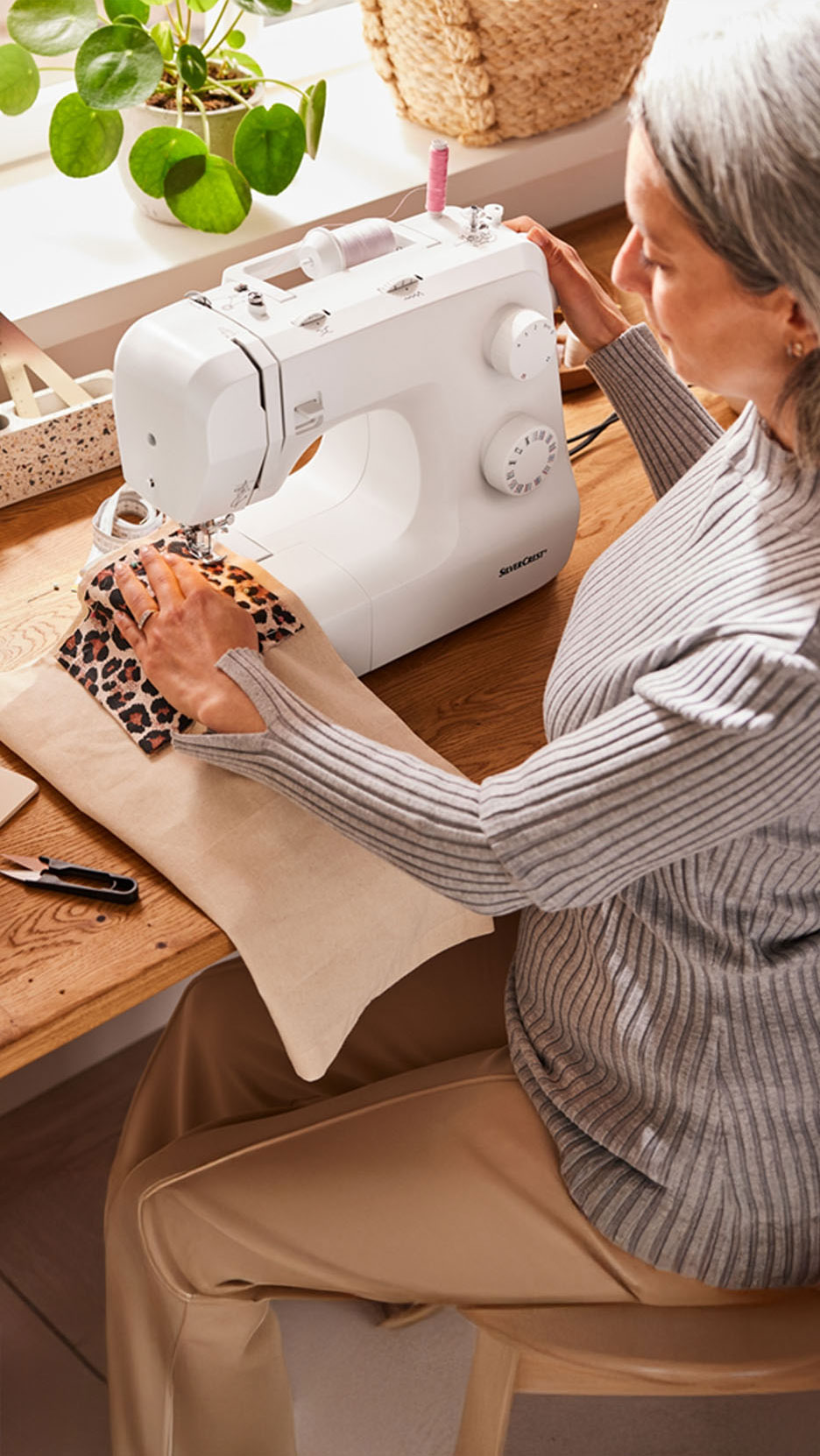 Une femme coud un tissu léopard sur une machine à coudre Silvercrest.