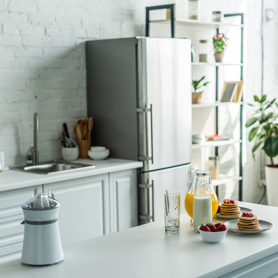 Sur un comptoir de cuisine, il y a un presse-agrumes, des carafes de lait et de jus d'orange, des crêpes et des fraises.