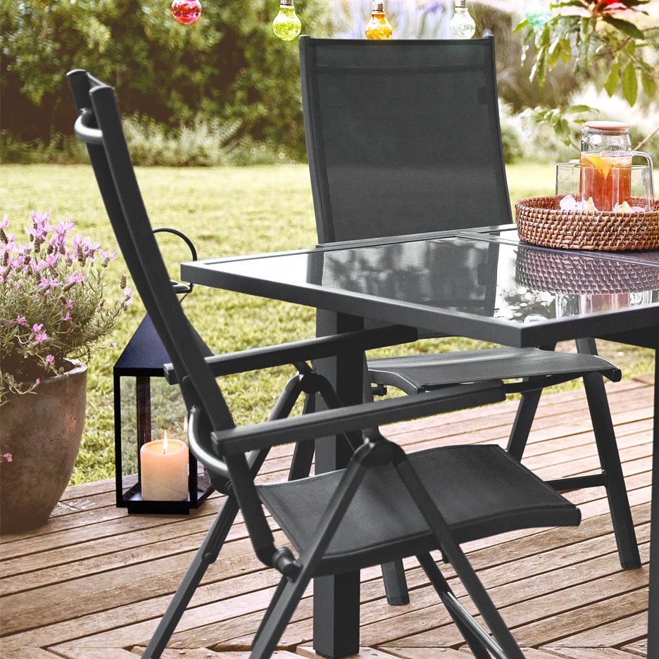 Um conjunto de mobiliário de jardim preto de metal e tecido com mesa de vidro numa varanda de madeira.