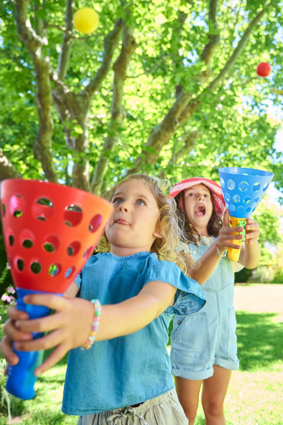 Deux jeunes filles jouent au jeu de lancer de balles avec des cornets en plastique colorés dans un jardin.