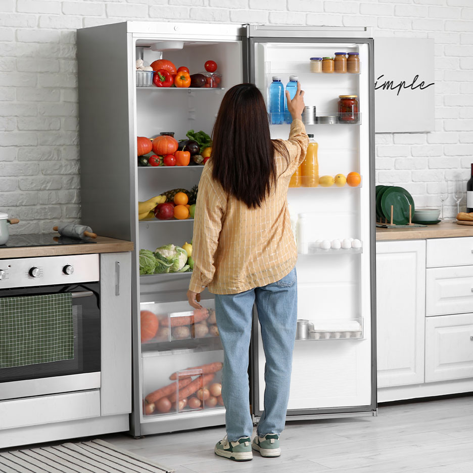 Femme prenant une bouteille d'eau dans un réfrigérateur rempli de fruits et légumes frais.