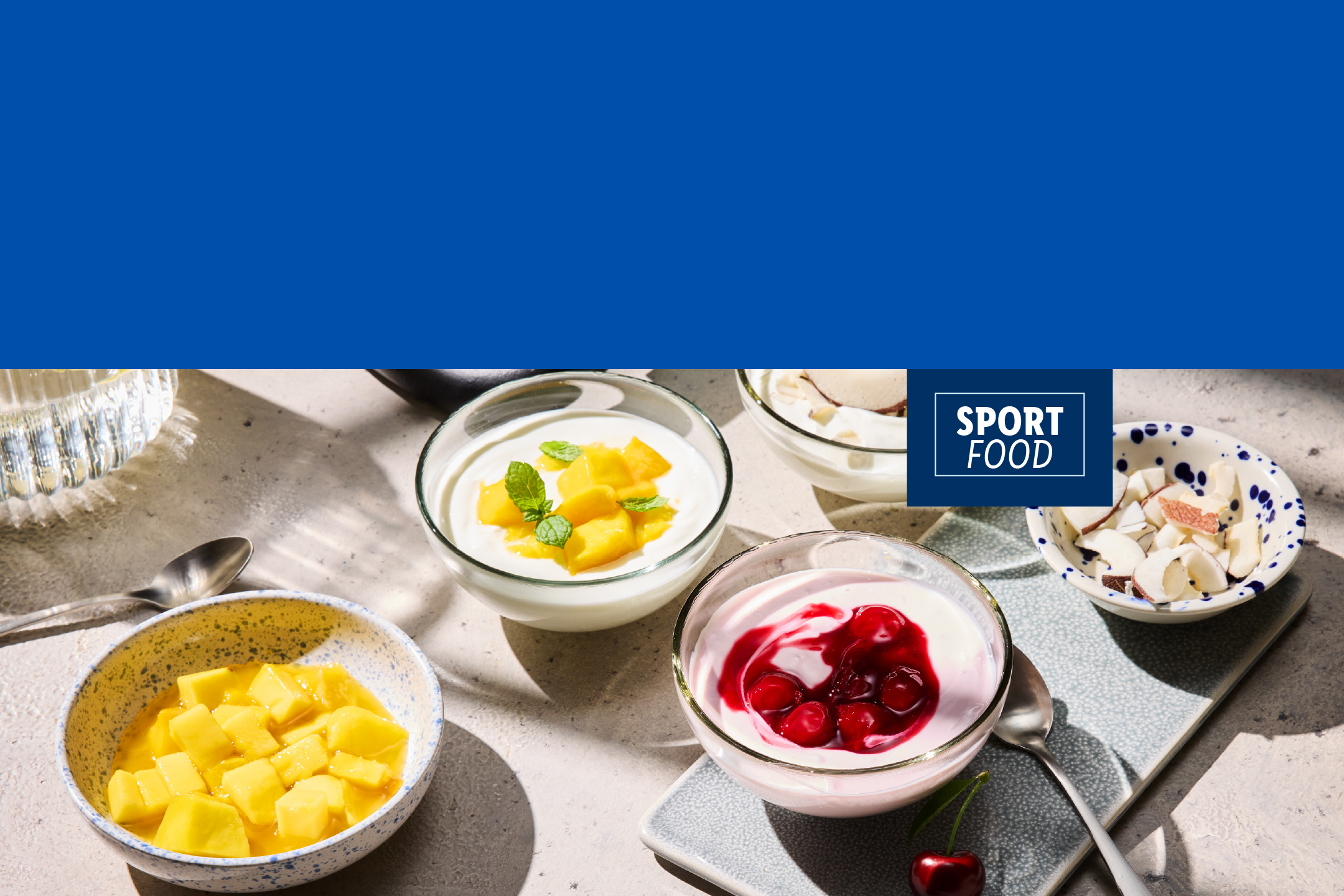 Yaourts avec fruits et noix, dont mangue et cerise, sur une table ensoleillée. Texte : SPORT FOOD.
