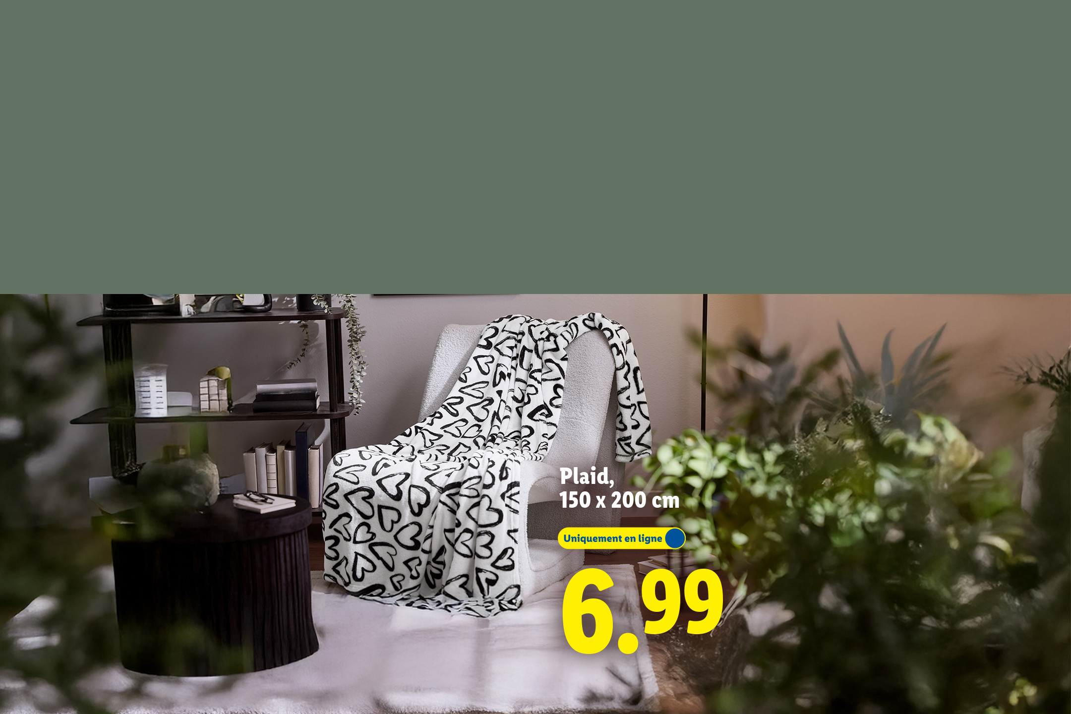 Plaid blanc à motifs cœurs noirs sur un fauteuil, avec une étagère et des plantes en arrière-plan. Prix : 6,99 €.