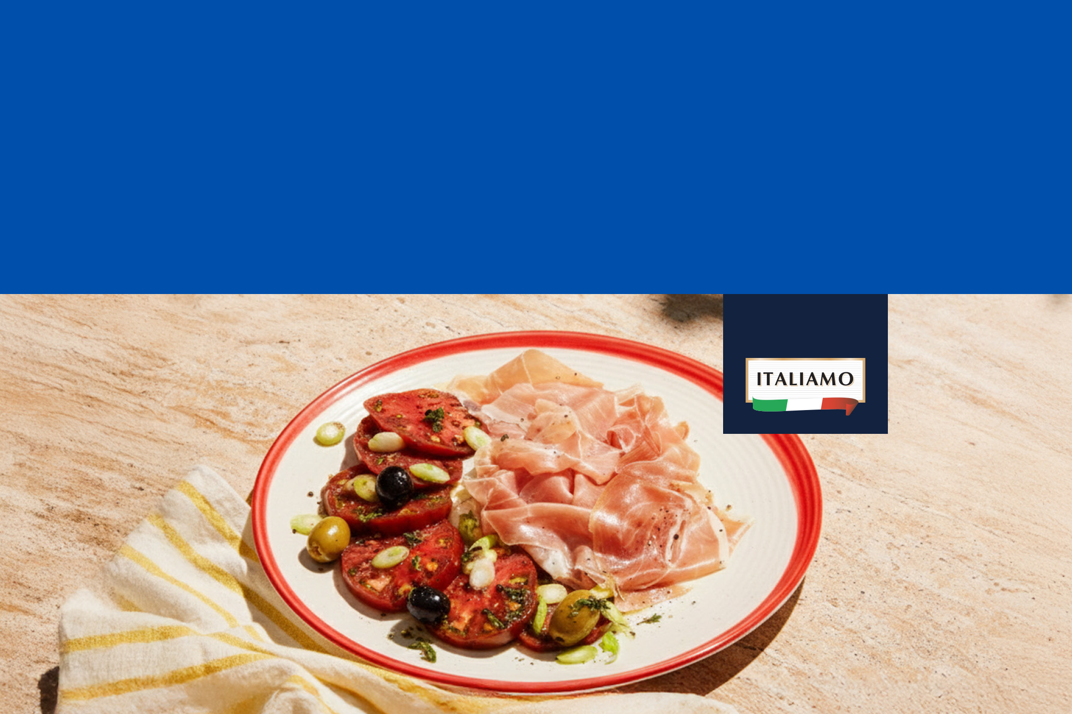 Assiette de tomates coupées, olives, oignons verts et jambon cru sur une table en pierre.