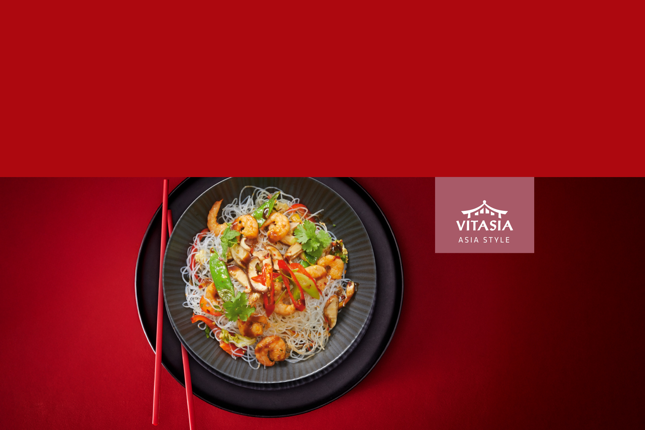 Nouilles de riz avec crevettes, légumes et champignons, accompagnées de baguettes rouges, sur fond rouge.