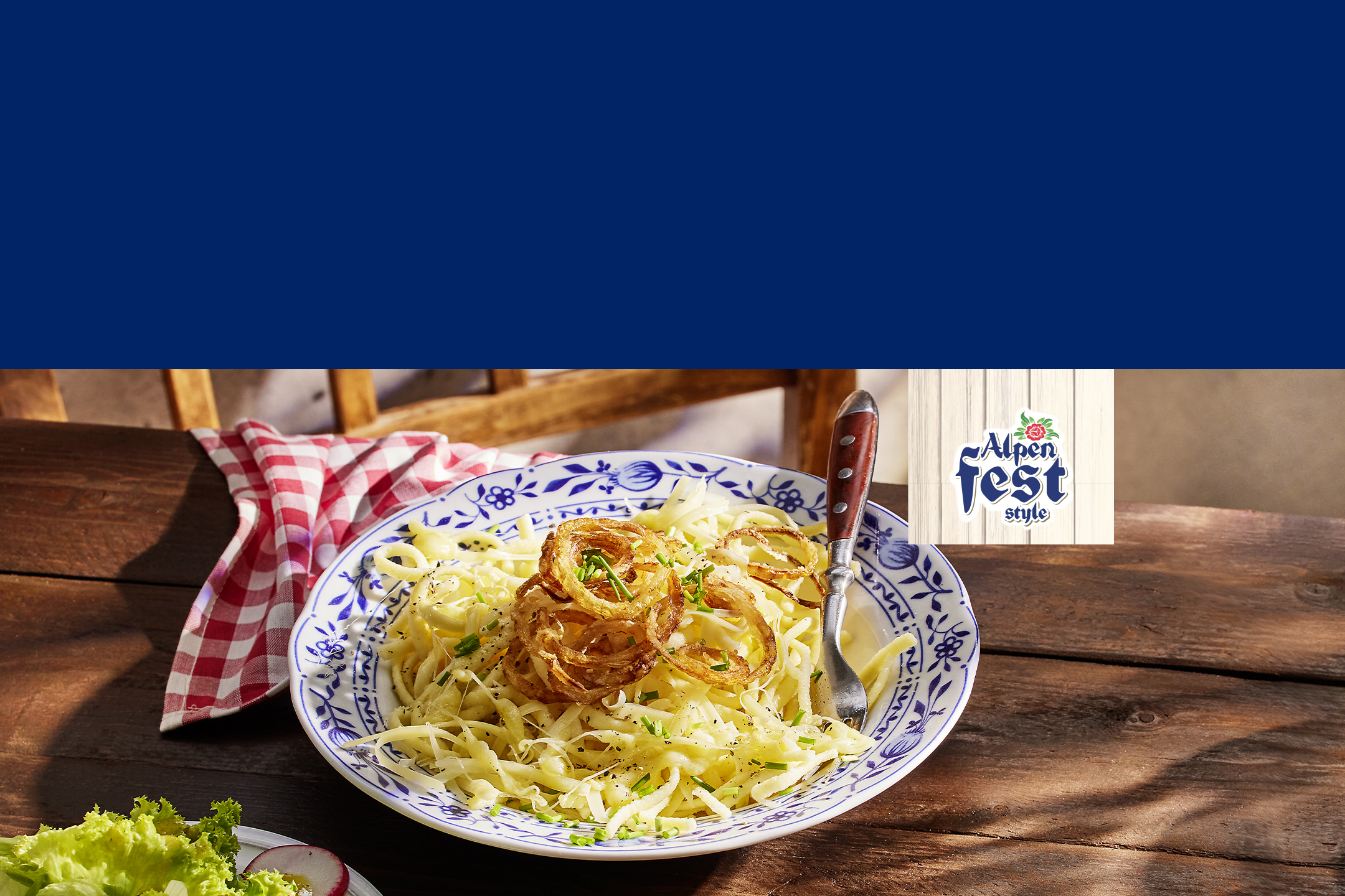 Plat de pâtes au fromage avec des oignons frits et une salade, style 'Alpen Fest'.