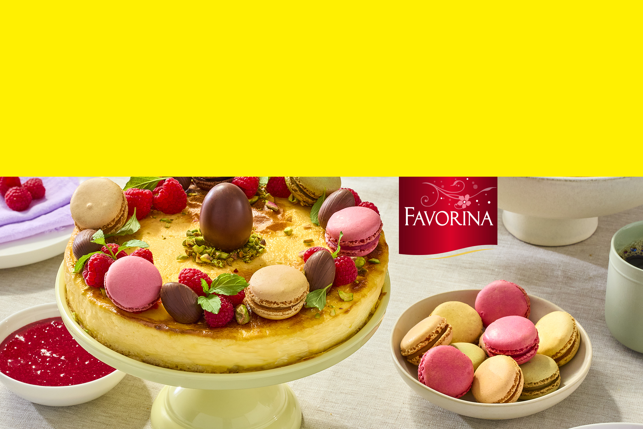 Cheesecake décoré de framboises, macarons et œufs en chocolat, avec un bol de macarons.