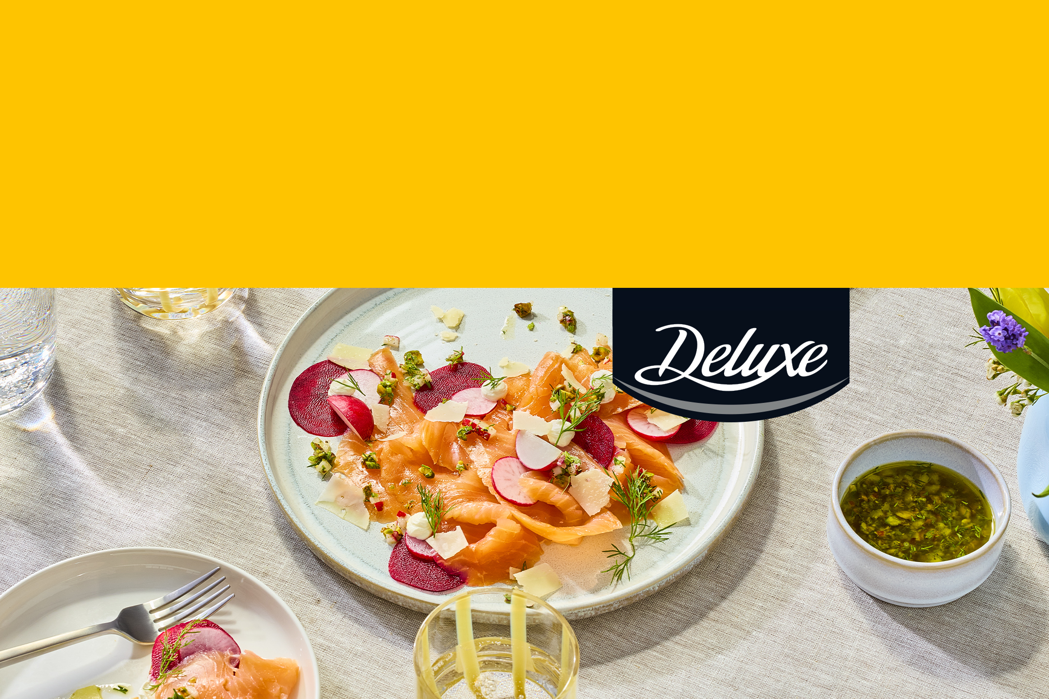 Plat de saumon fumé avec betteraves, radis et sauce verte, sur une table avec des verres.