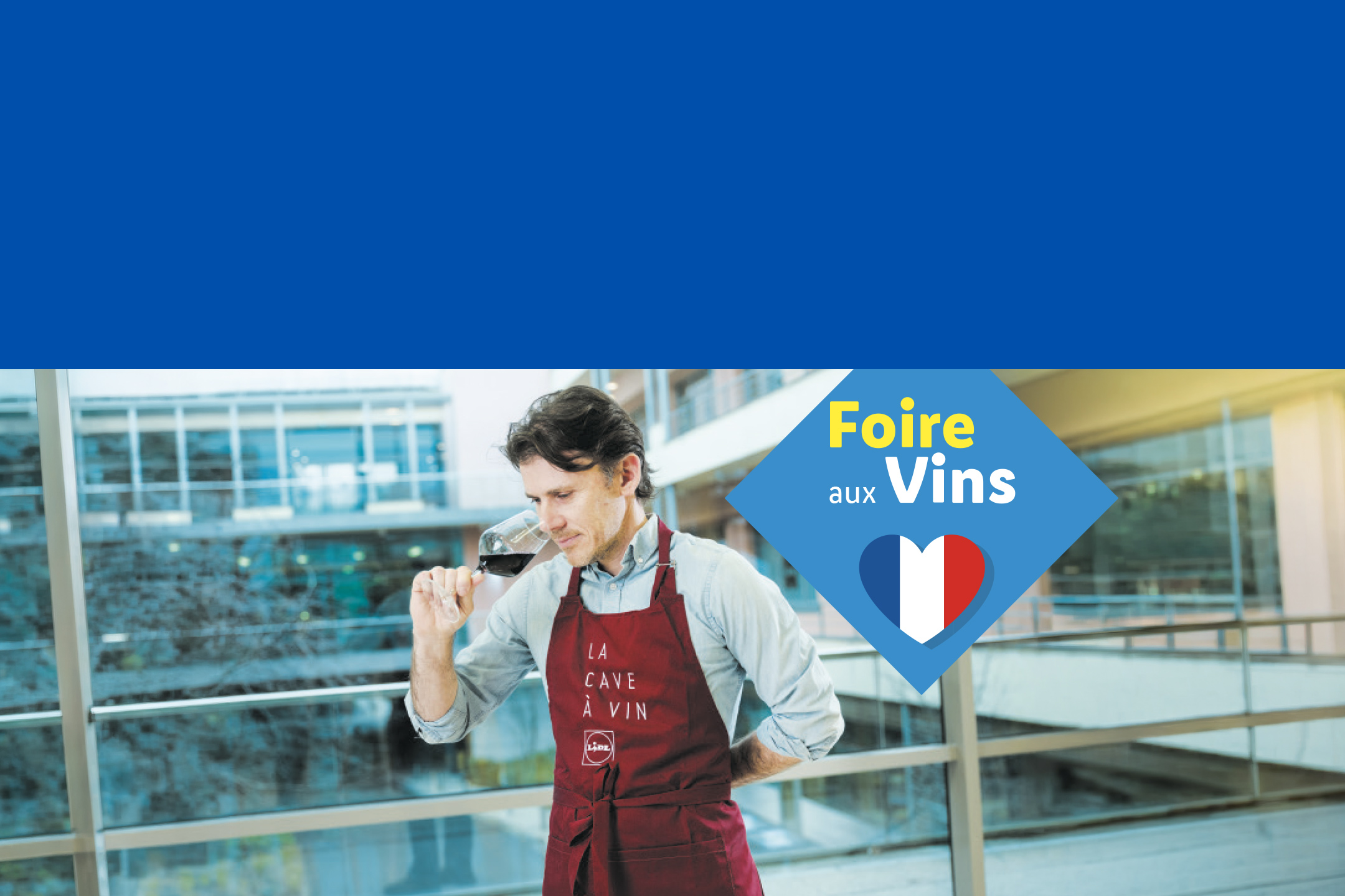 Un homme en tablier de sommelier sentant du vin, avec un logo 'Foire aux Vins' et un cœur aux couleurs françaises.