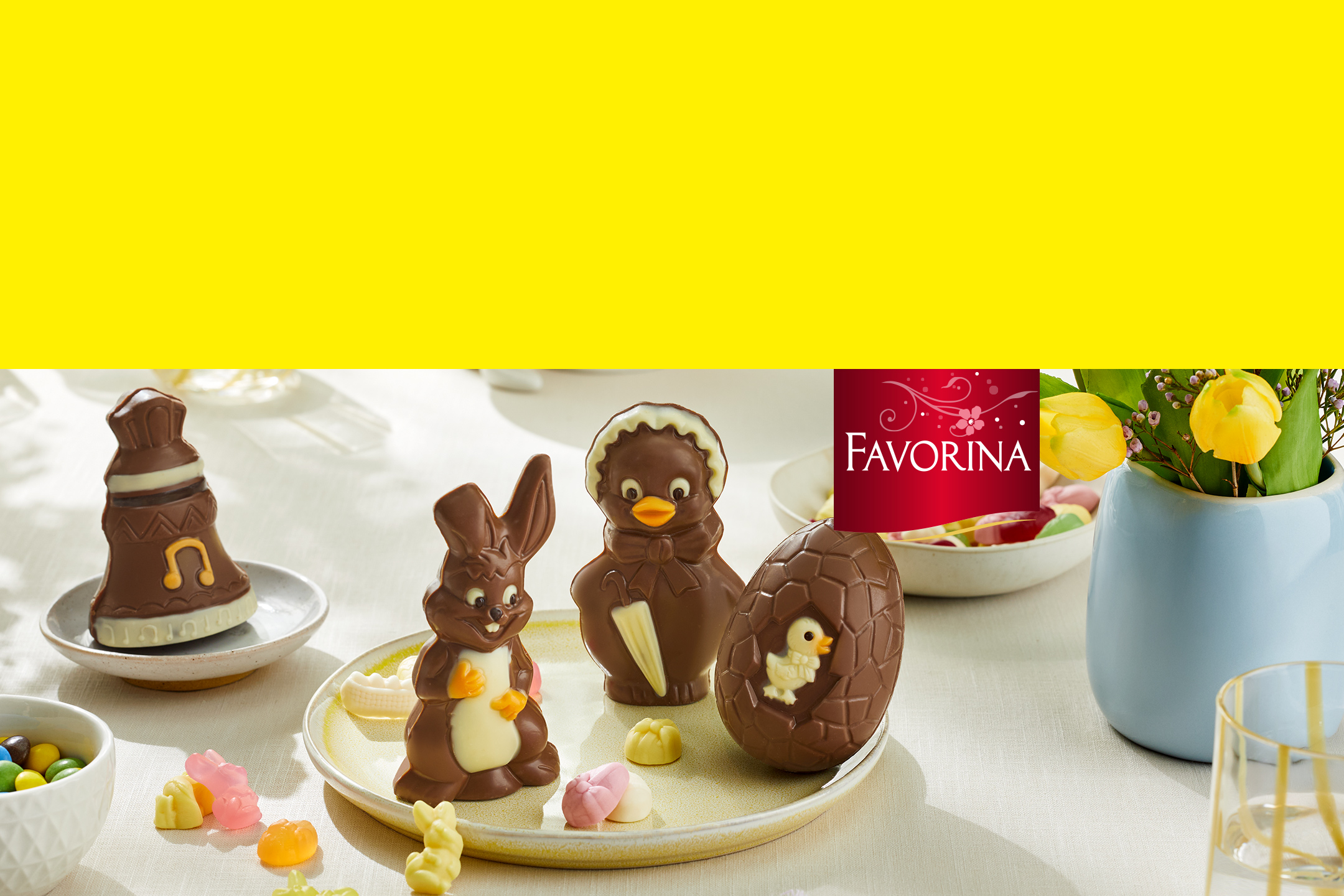 Chocolats de Pâques en forme de lapin, poussin et œuf, avec des bonbons et des fleurs.