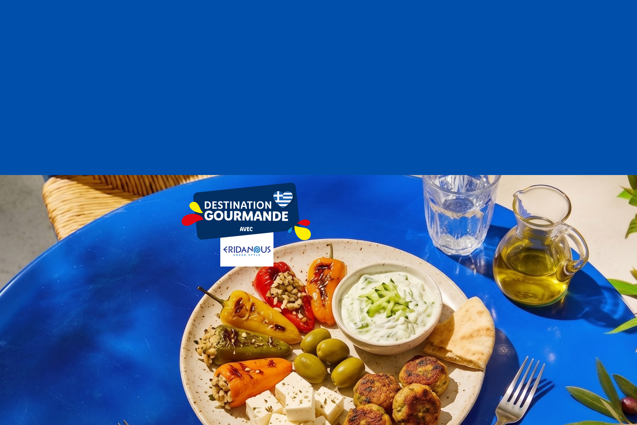 Assiette grecque avec poivrons farcis, tzatziki, feta, olives et boulettes, sur une table bleue.